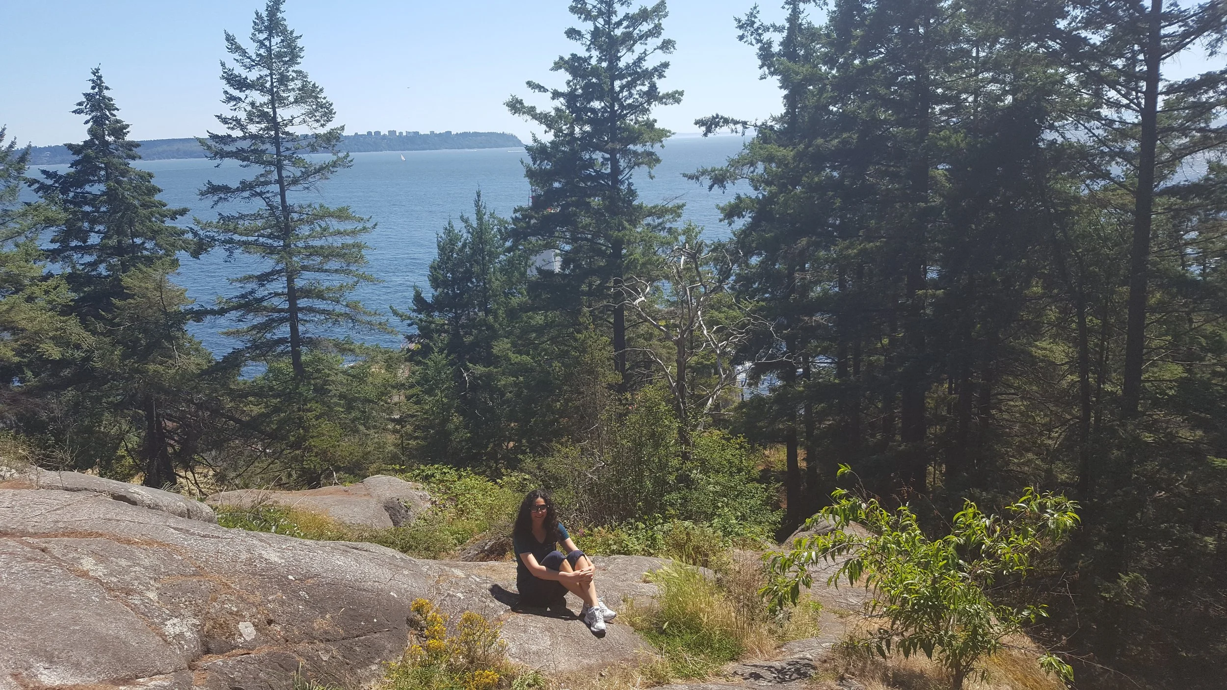 Stasha is sitting on the rock with the ocean in the background.