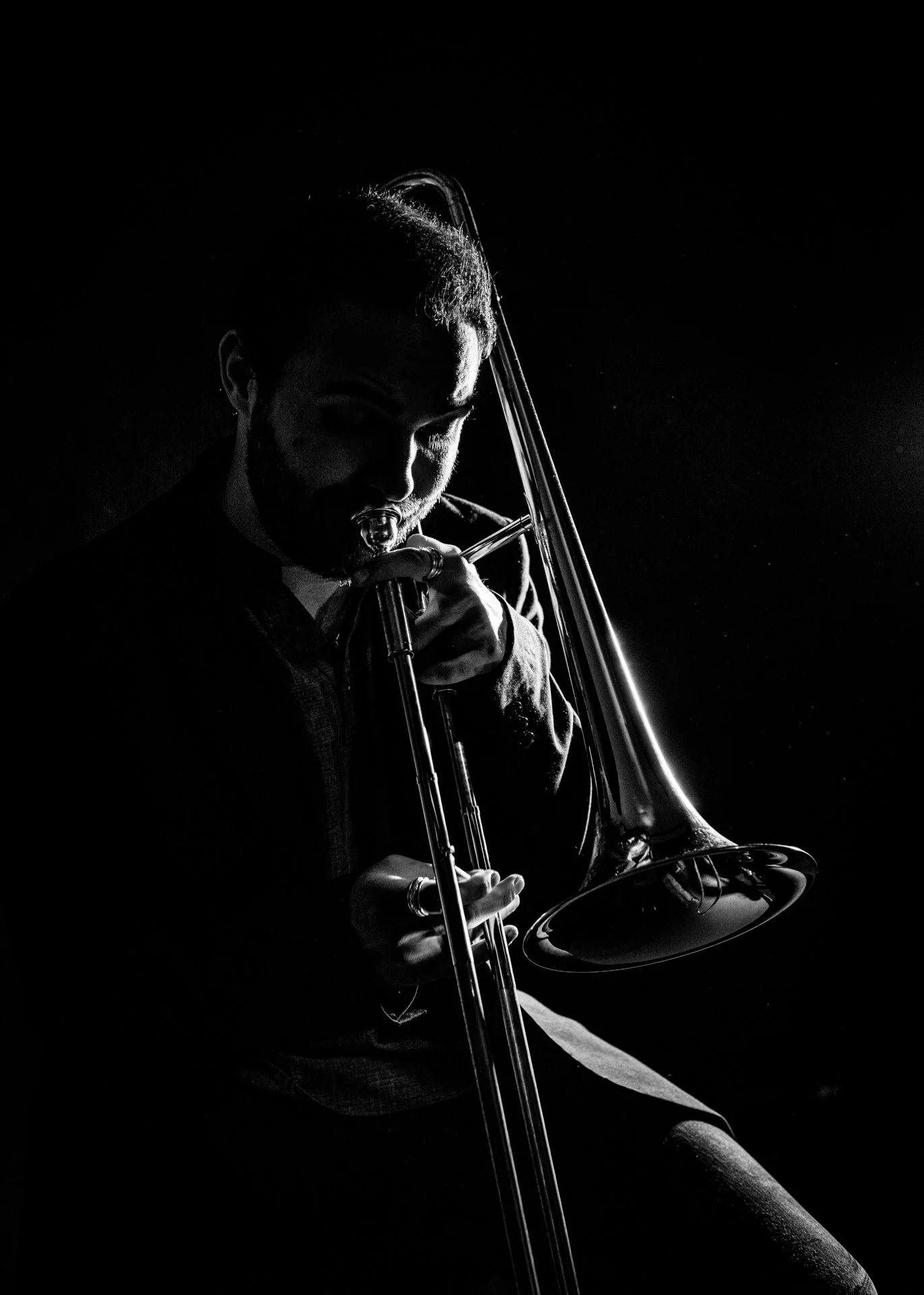 Hombre tocando el trombón en un estilo en blanco y negro con iluminación dramática.