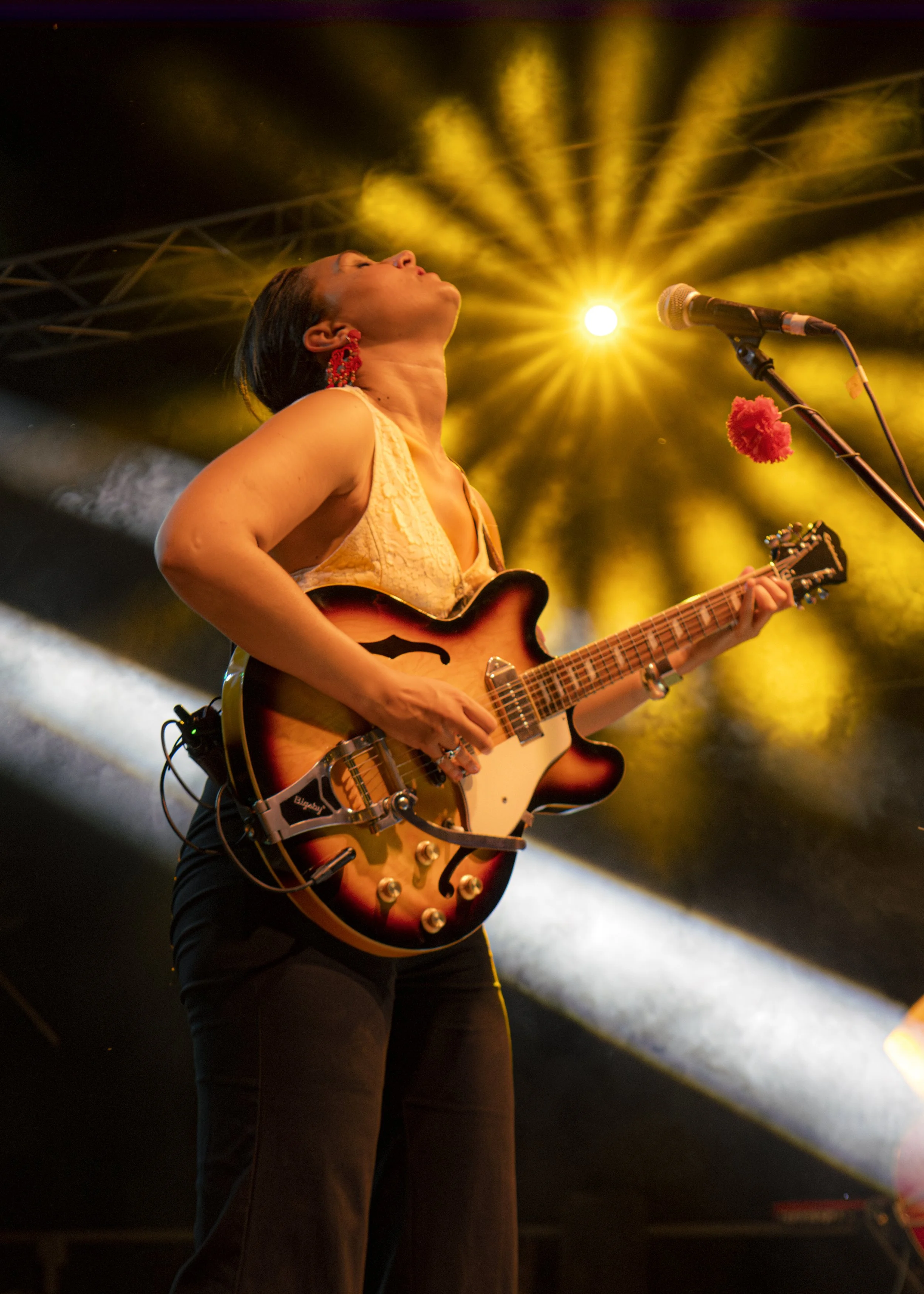 Mujer tocando guitarra eléctrica en un escenario con iluminación amarilla y humo.