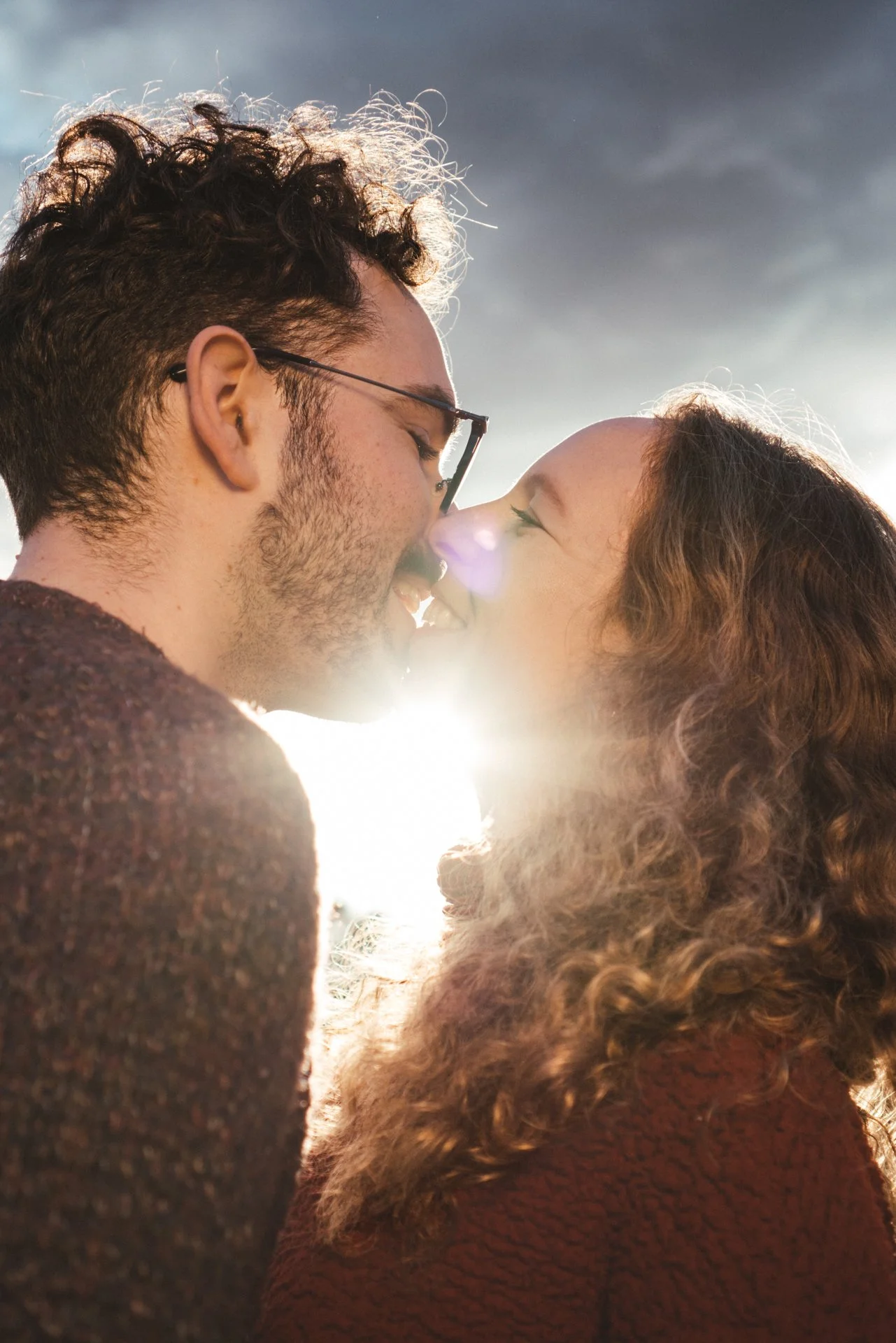 Una pareja joven se está besando con el sol detrás de ellos.