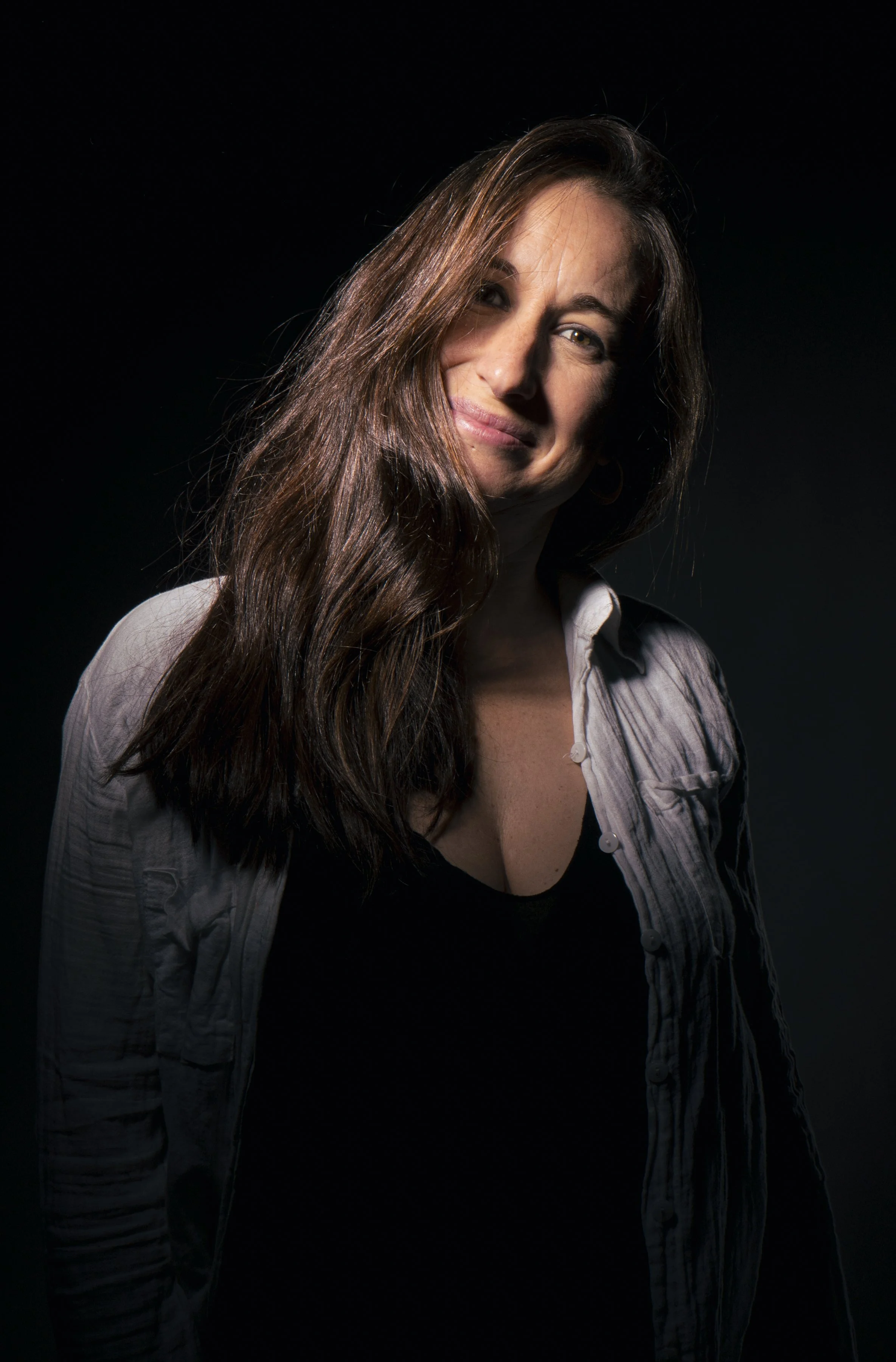 Retrato de una mujer con cabello largo y castaño, sonriendo ligeramente, con fondo oscuro.