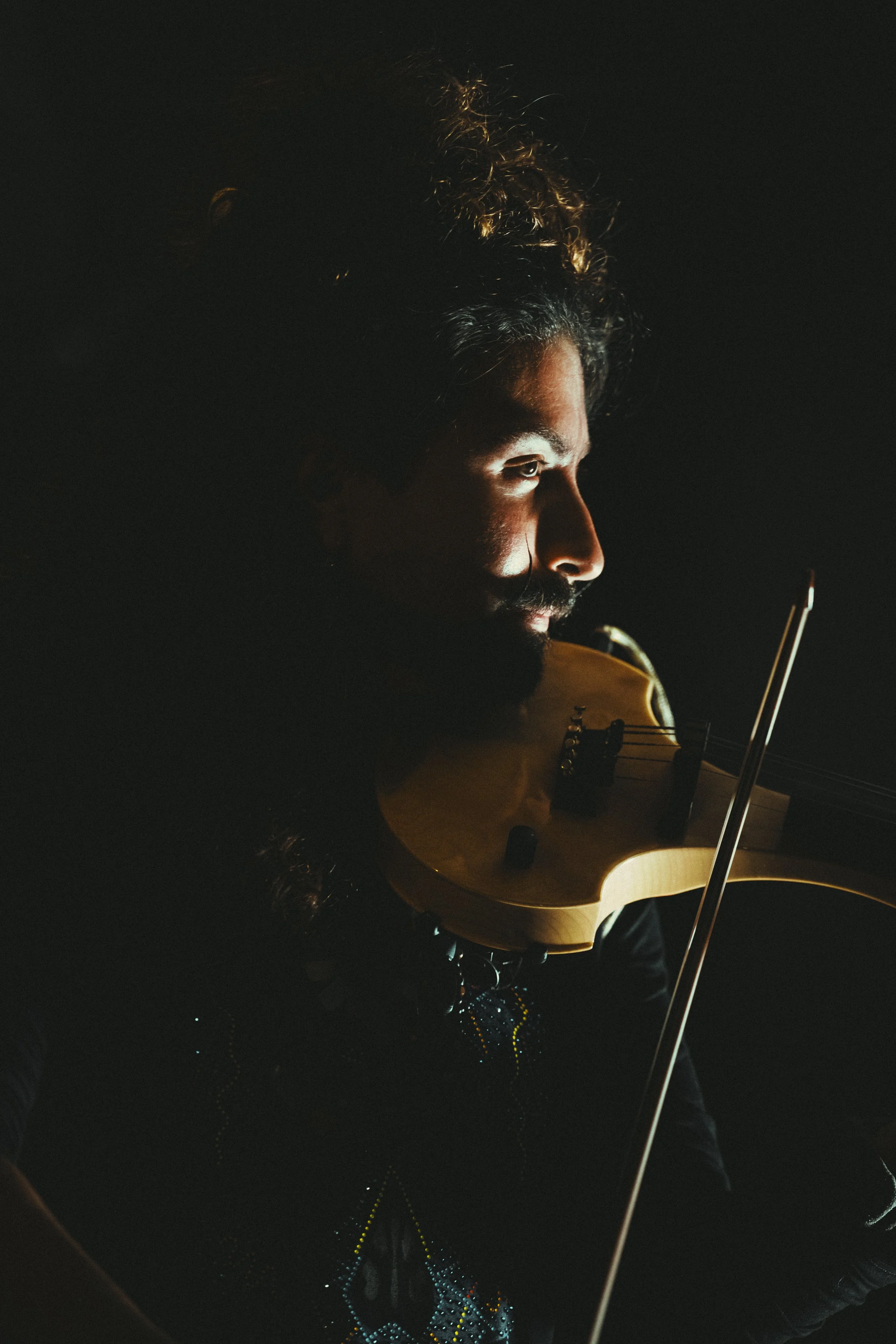 Hombre tocando el violín en un escenario oscuro, con iluminación enfocada en su rostro y violín.