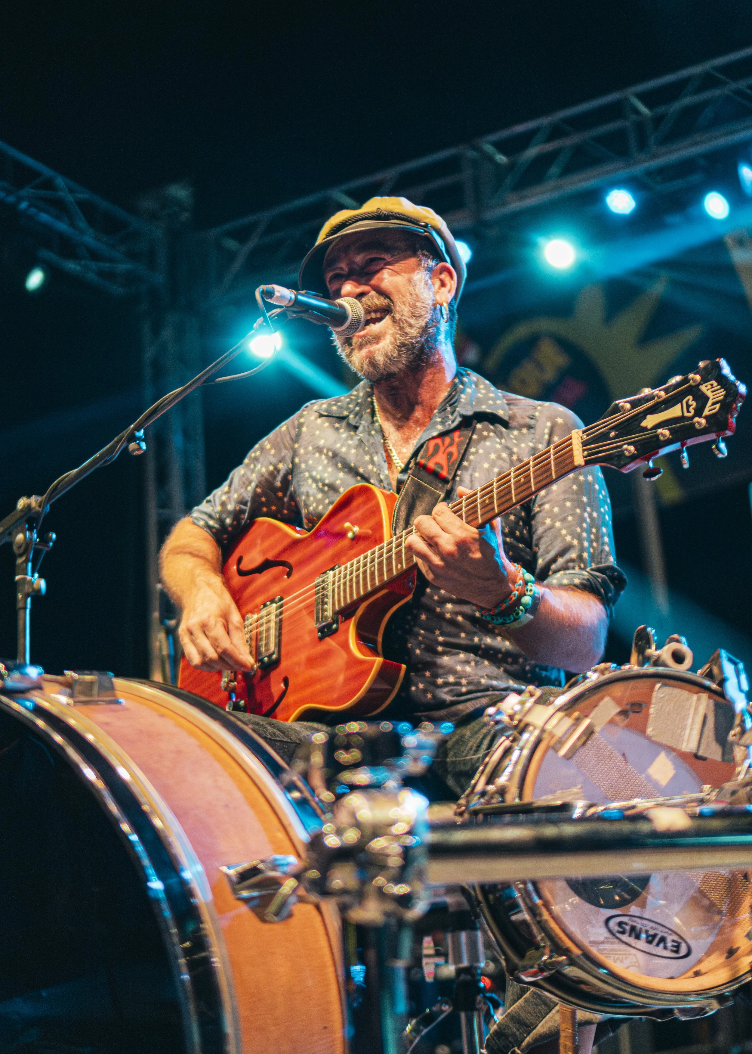 Hombre tocando guitarra eléctrica y cantando con micrófono en escenario con luces azules.