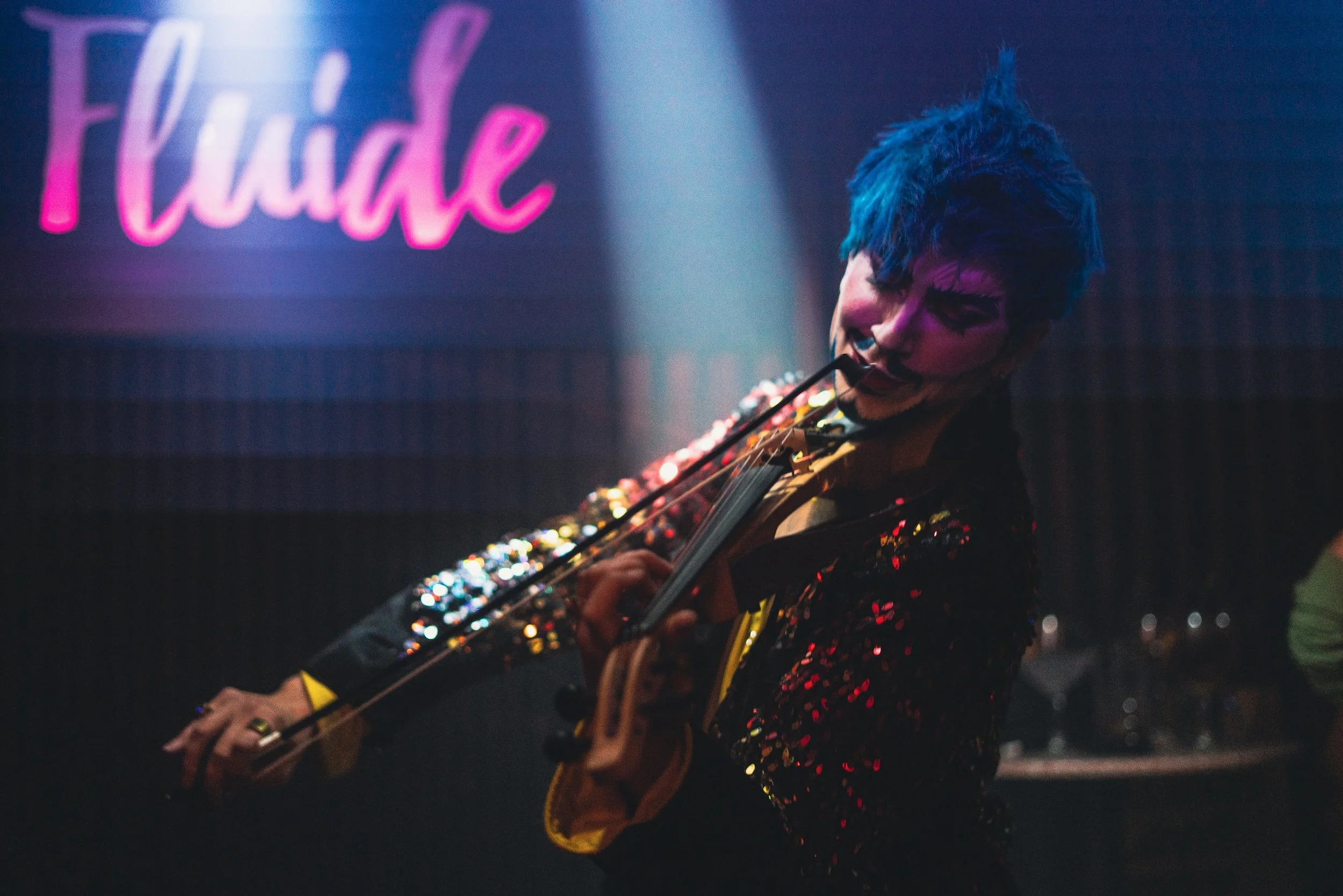 Persona tocando guitarra en un escenario con letrero rosa y azul que dice 'Fluid'.