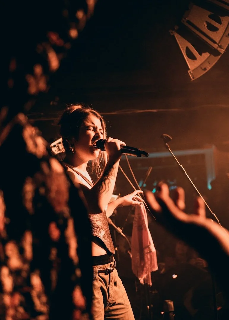 Mujer cantando en un concierto con iluminación cálida y un micrófono en mano.