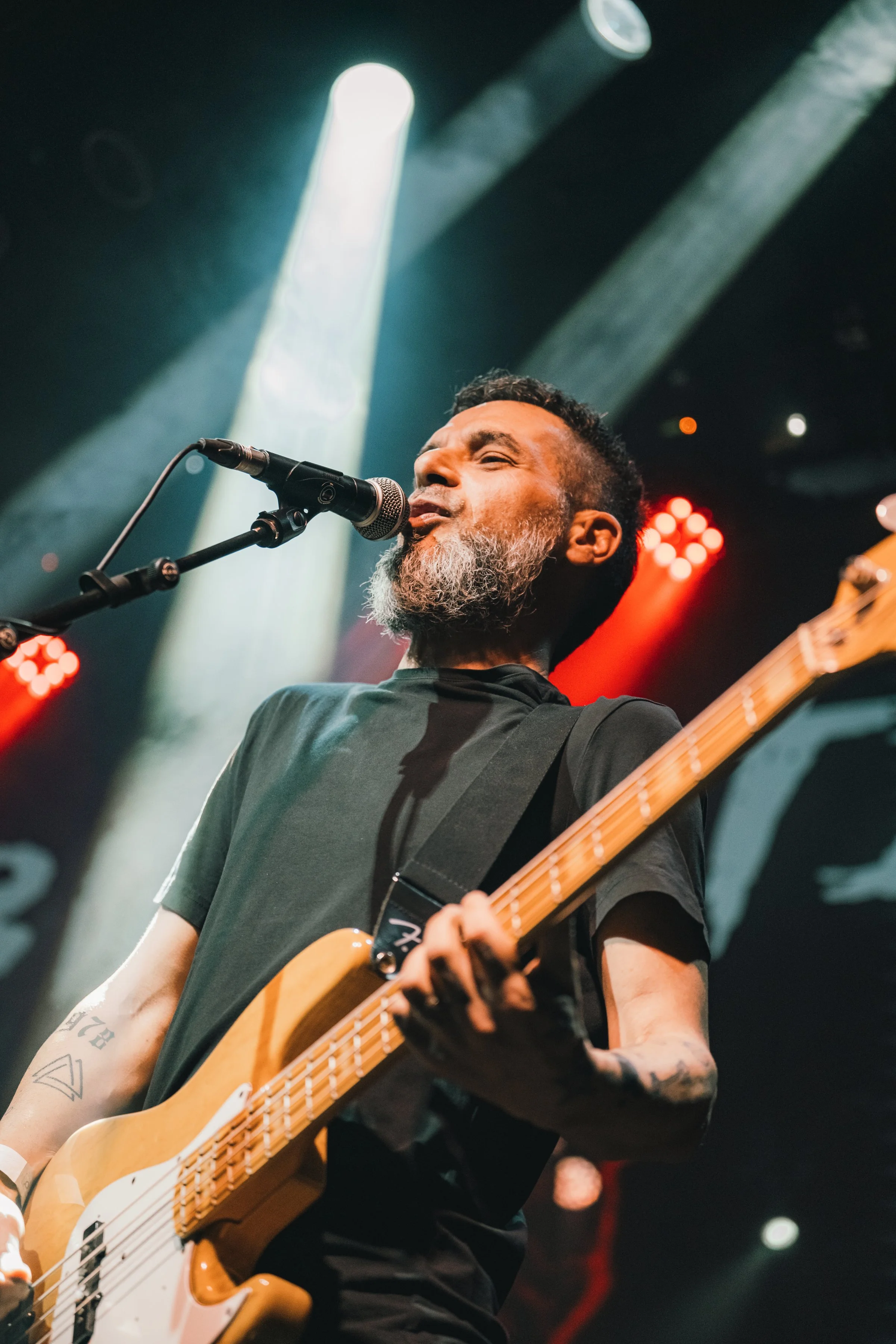 Hombre tocando la guitarra eléctrica y cantando en un concierto, con luces de escenario coloridas en el fondo.