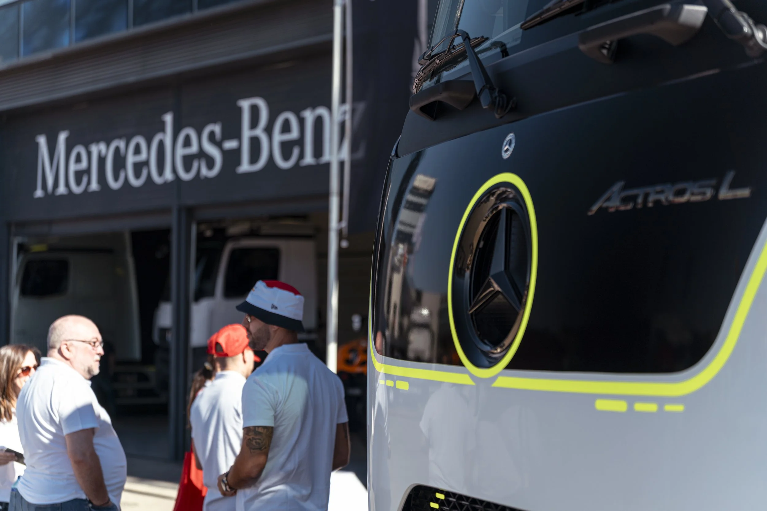 Grupo de personas conversando frente a un edificio de Mercedes-Benz, con un autobús Mercedes-Benz en primer plano.