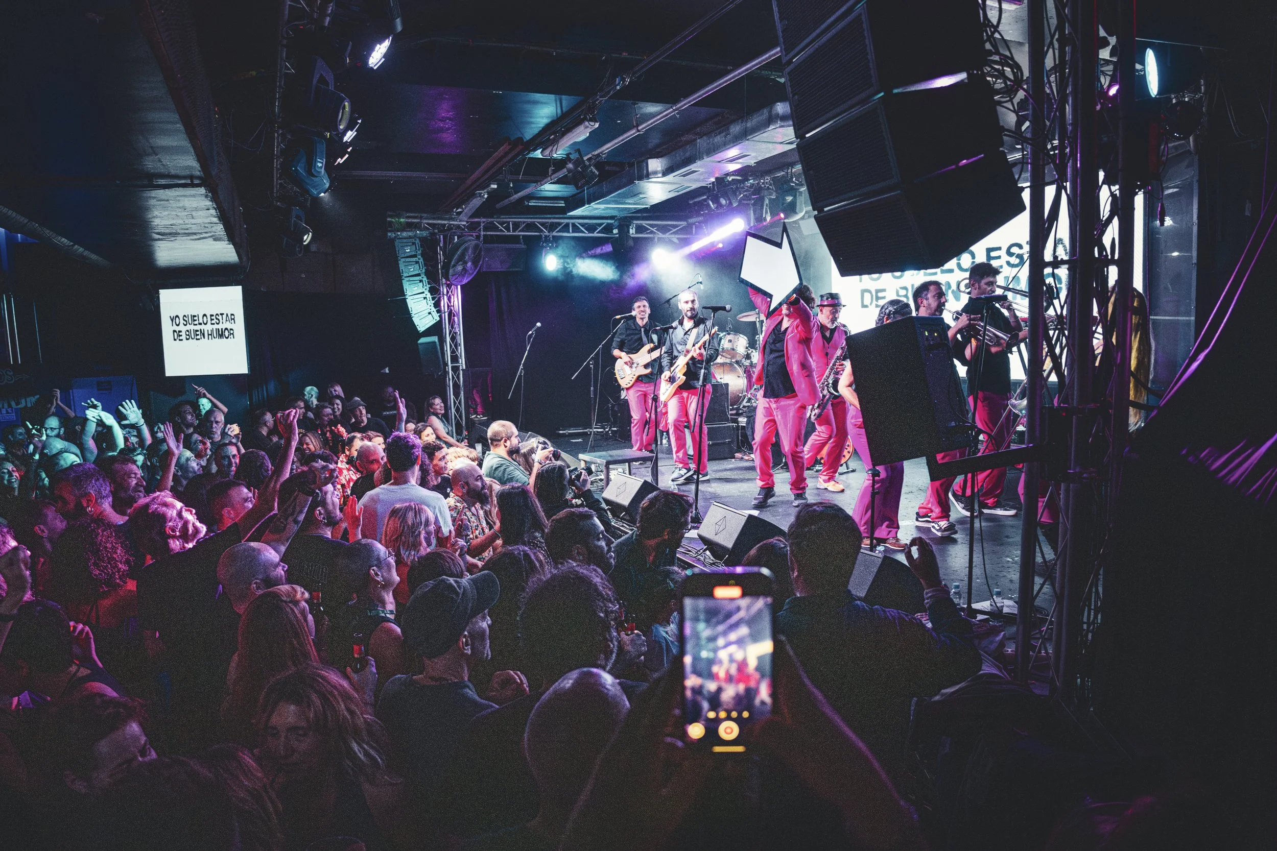 Concierto con banda tocando en escenario, público disfrutando y tomando fotos.