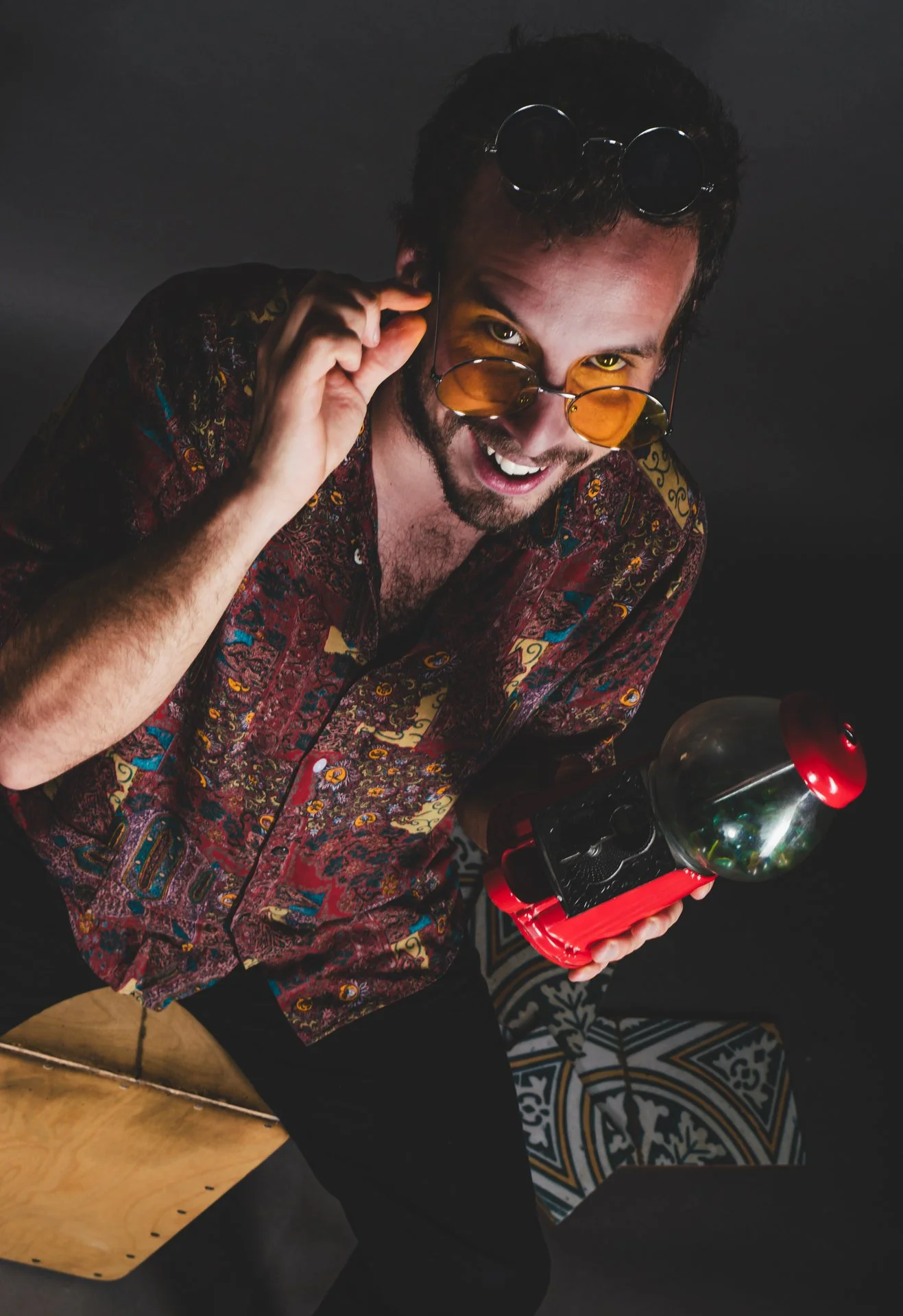 Hombre con gafas de sol amarillas, vestido con camisa de patrón colorido, sosteniendo una máquina del tiempo y sonriendo.