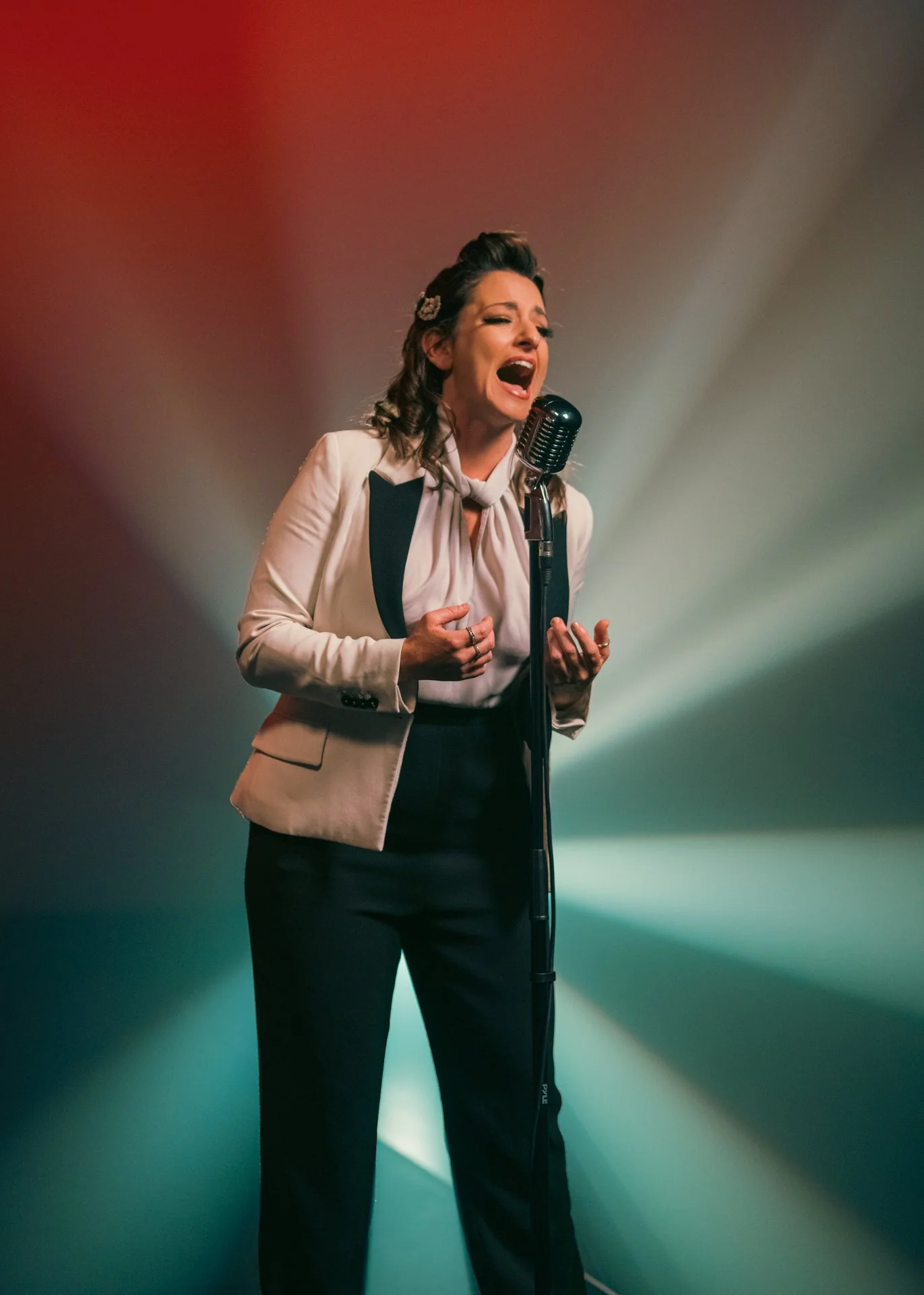 Mujer cantando frente a un micrófono en un escenario con iluminación de fondo colorida.
