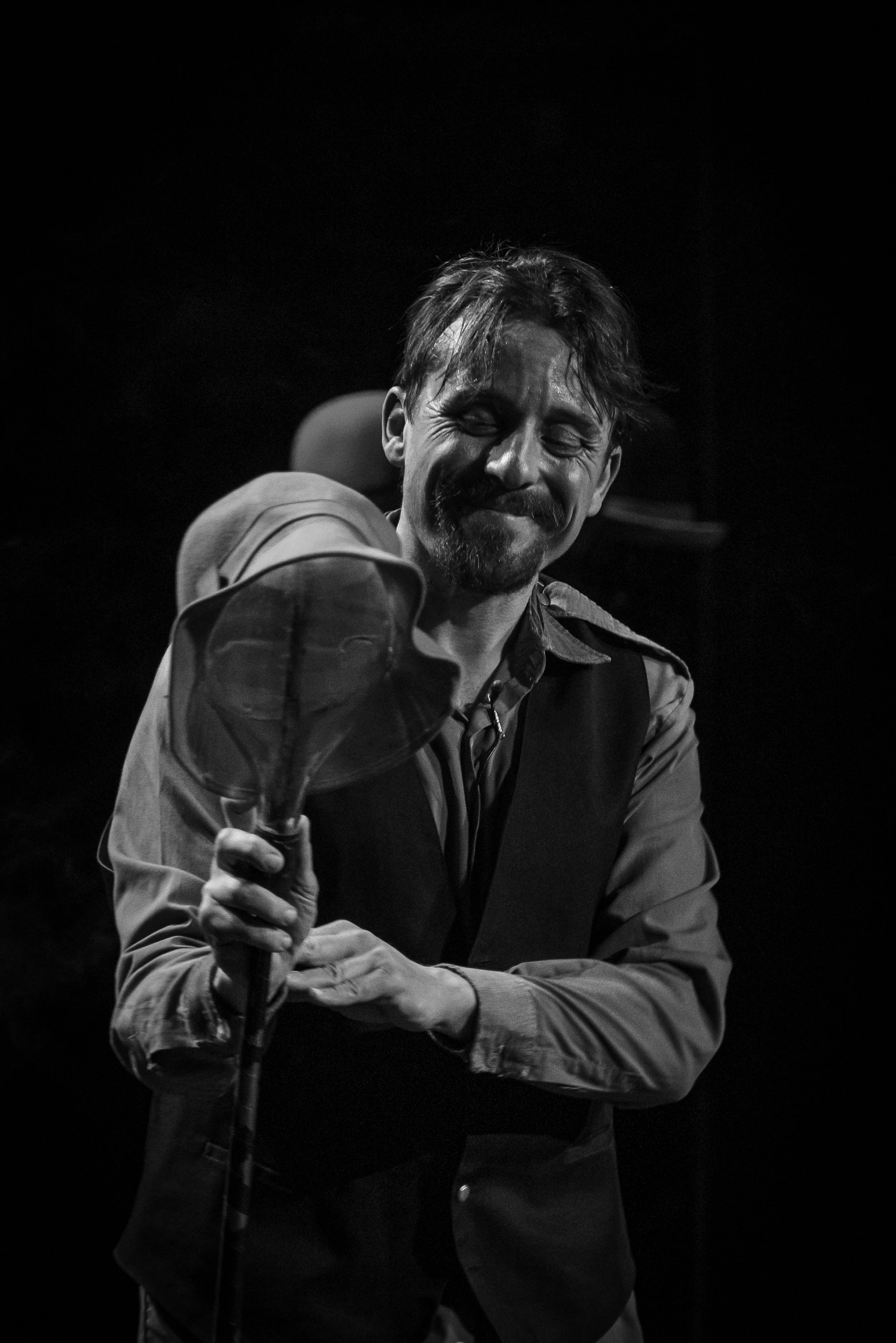 Hombre sonriente con bigote y barba, sosteniendo un sombrero, en blanco y negro.