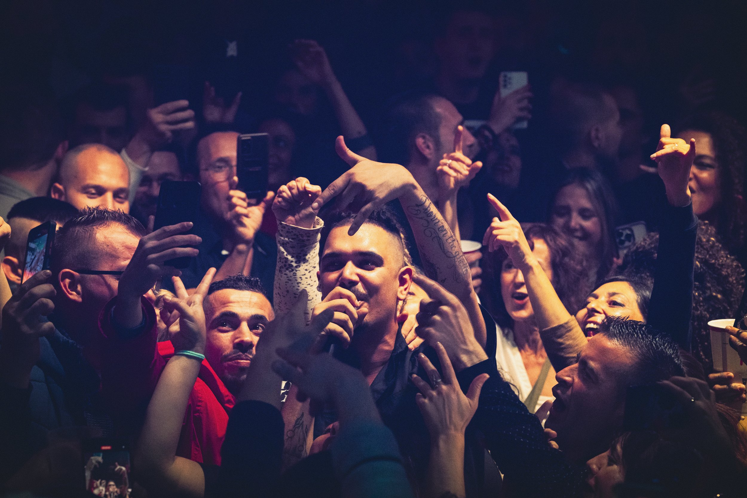 Un grupo de personas disfrutando y tomando fotos en una fiesta o concierto, con un hombre en el centro en medio del público.