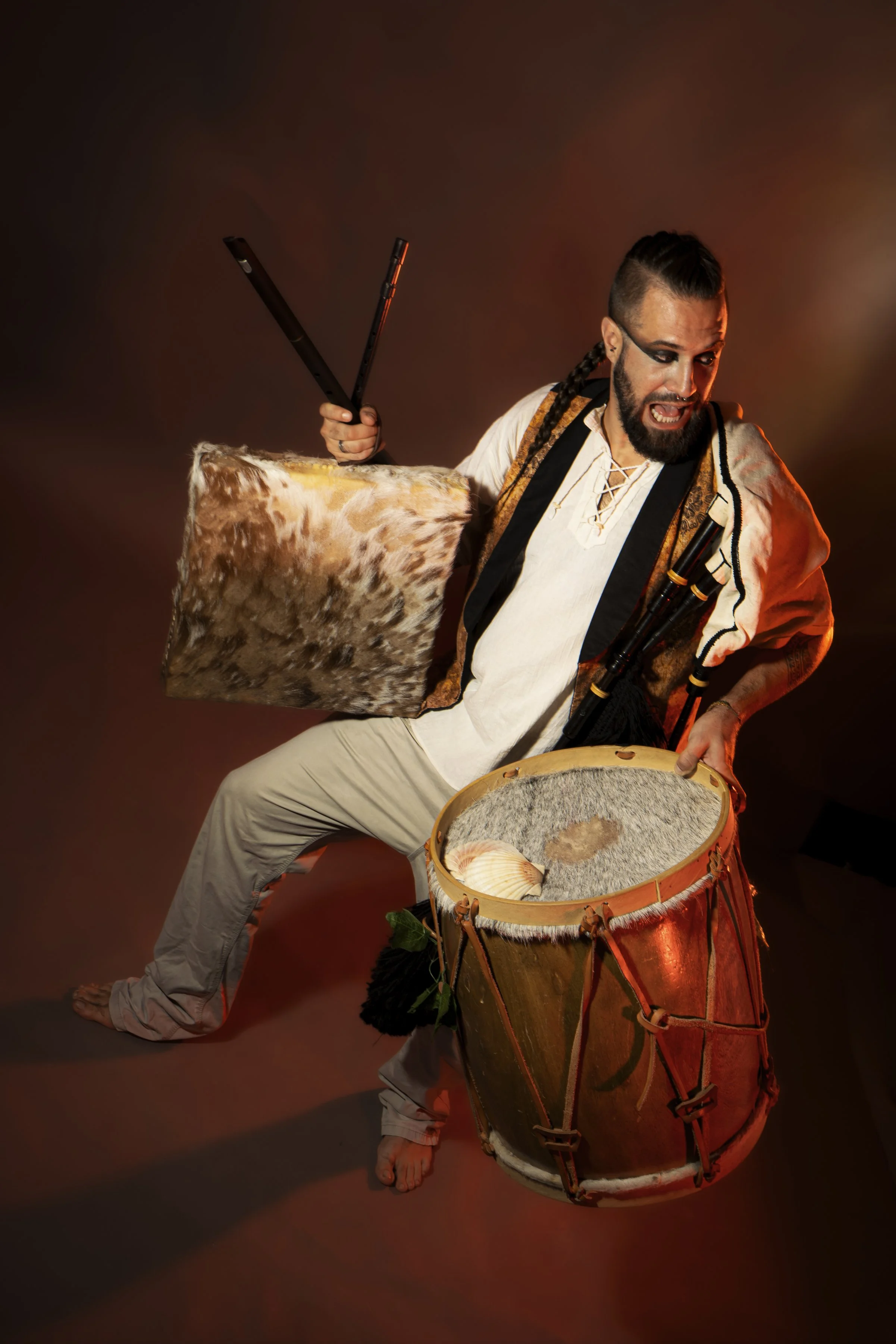 Un hombre con maquillaje y peinado tribal tocando un tambor grande y una caja con un bate de béisbol.