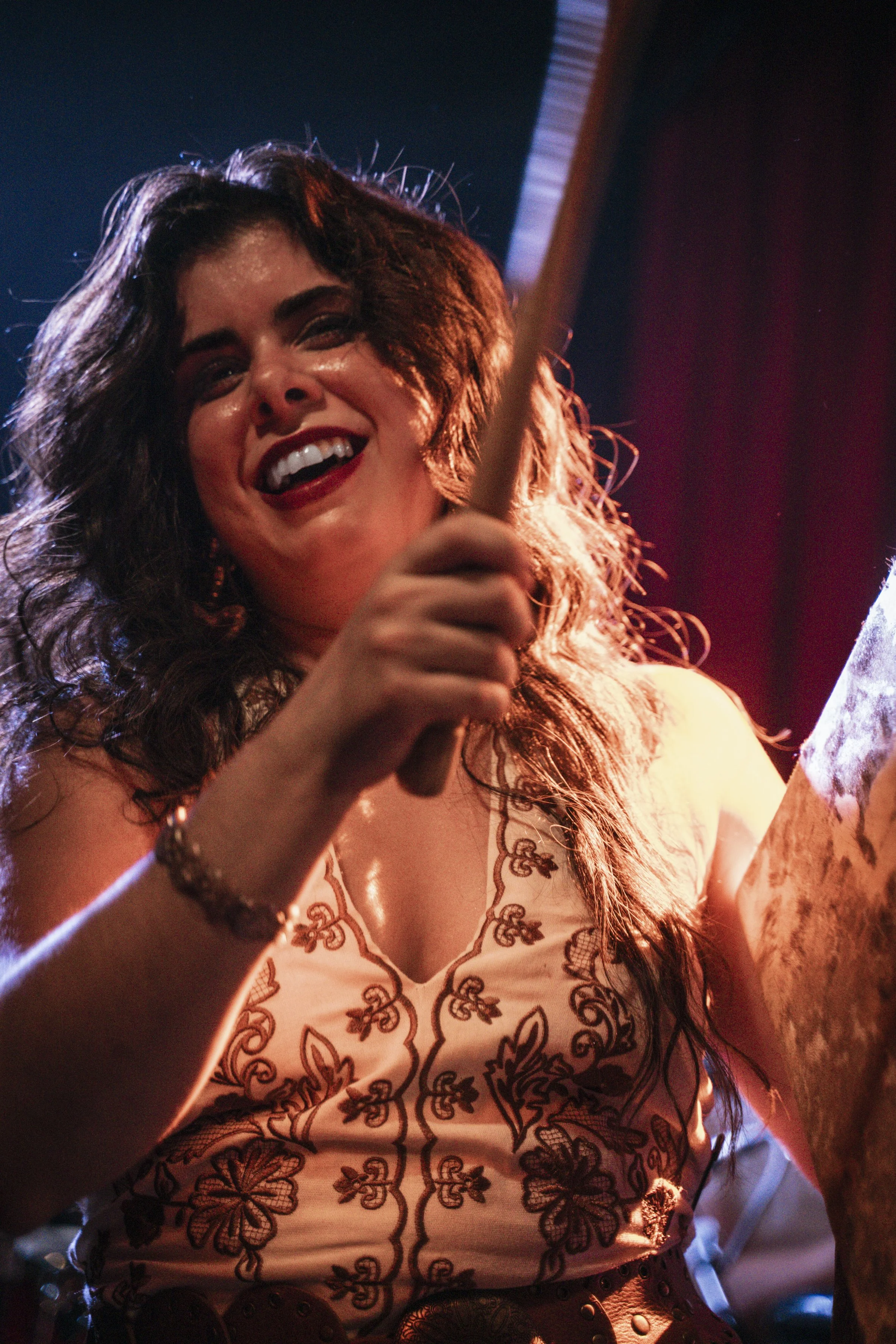 Mujer sonriendo y tocando un instrumento musical en un escenario con barbas de luz roja y azul.