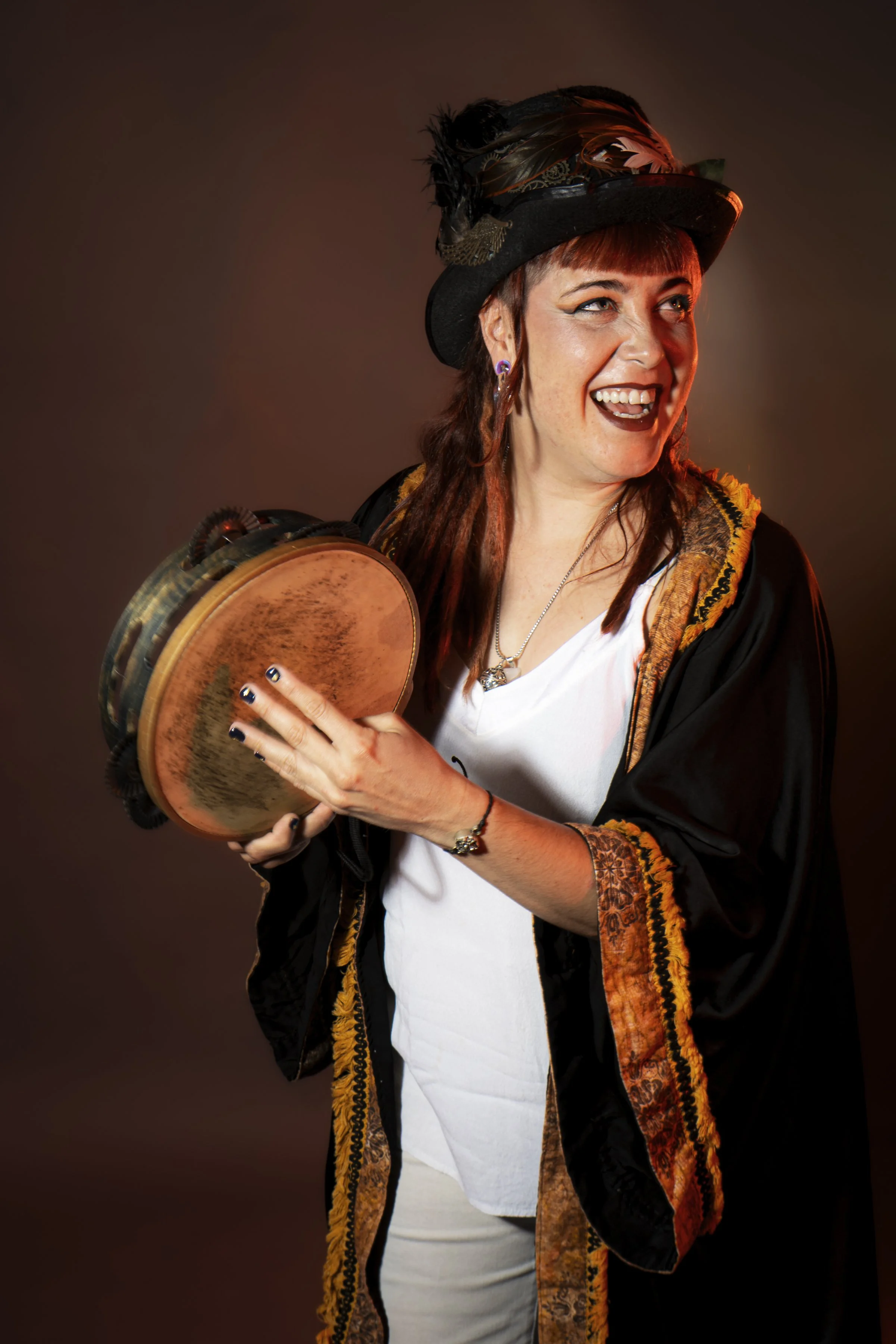 Mujer con sombrero, vestimenta elegante, sosteniendo un instrumento de percusión, sonriendo y mirando hacia un lado.