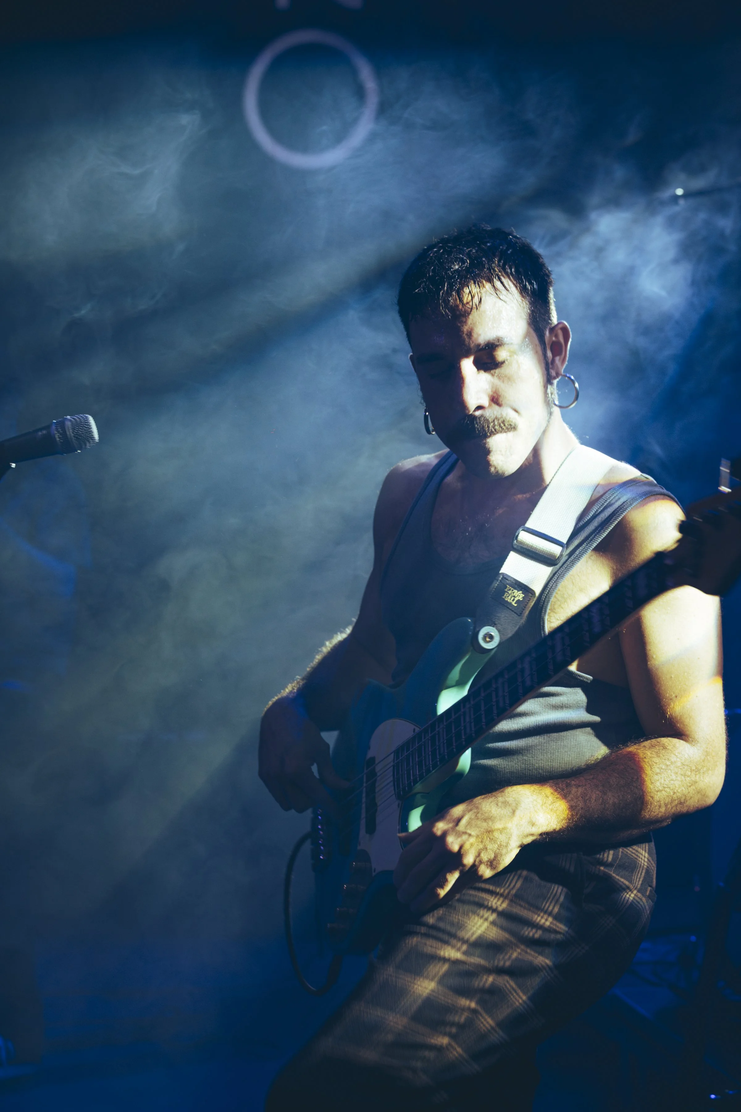 Un hombre tocando guitarra eléctrica en concierto, con luz de escenario azul y humo de fondo.