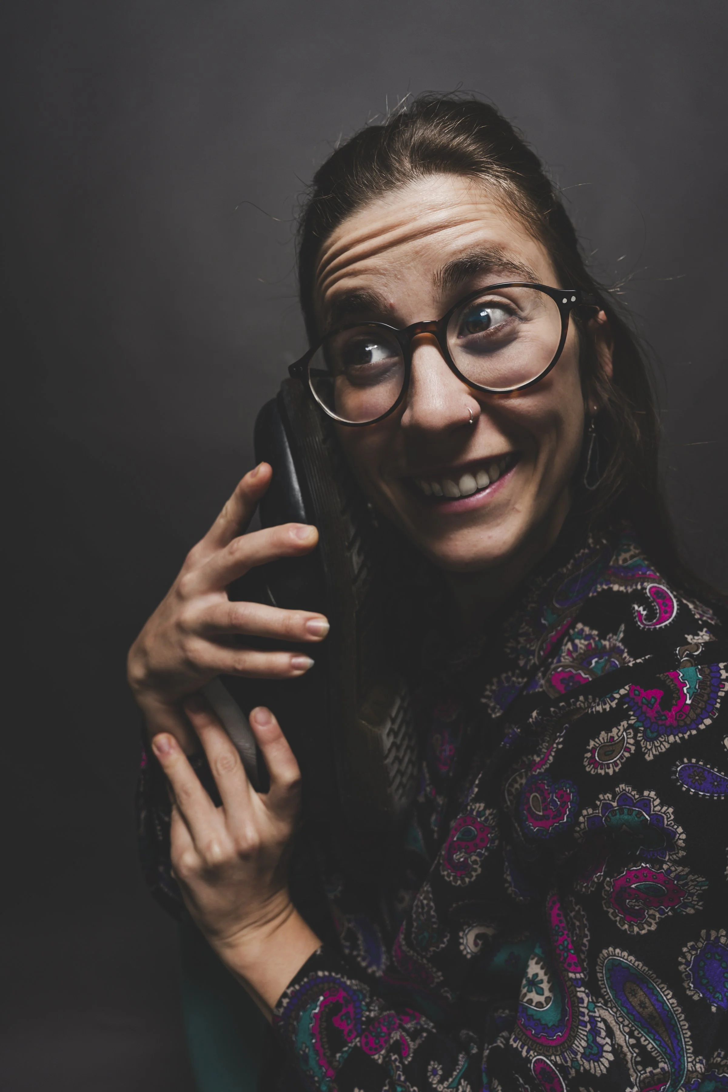 Mujer con gafas y peinado recogido, sonriendo mientras habla por teléfono, vistiendo una blusa con estampado de colores