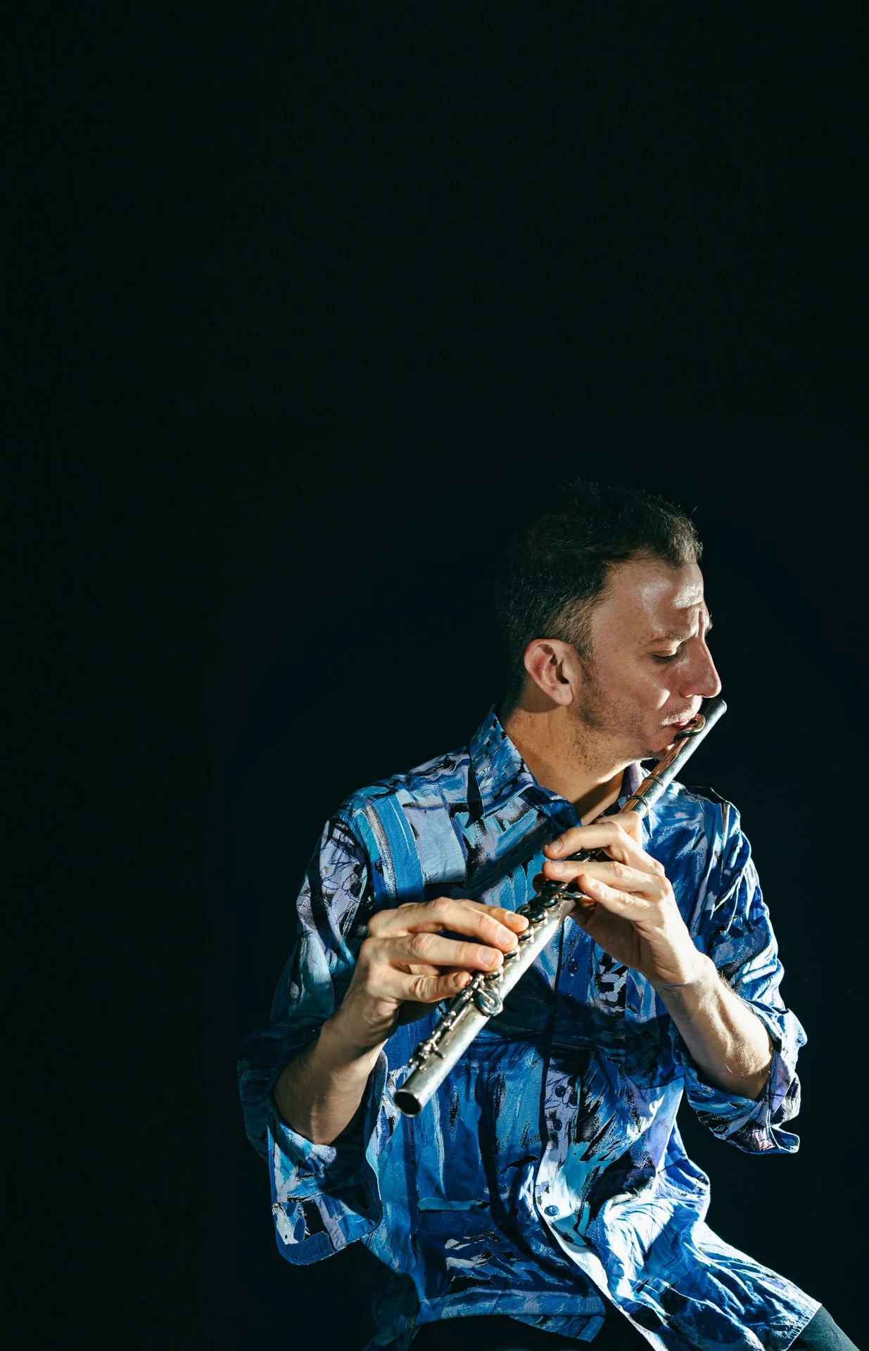 Hombre tocando la flauta en un fondo negro.