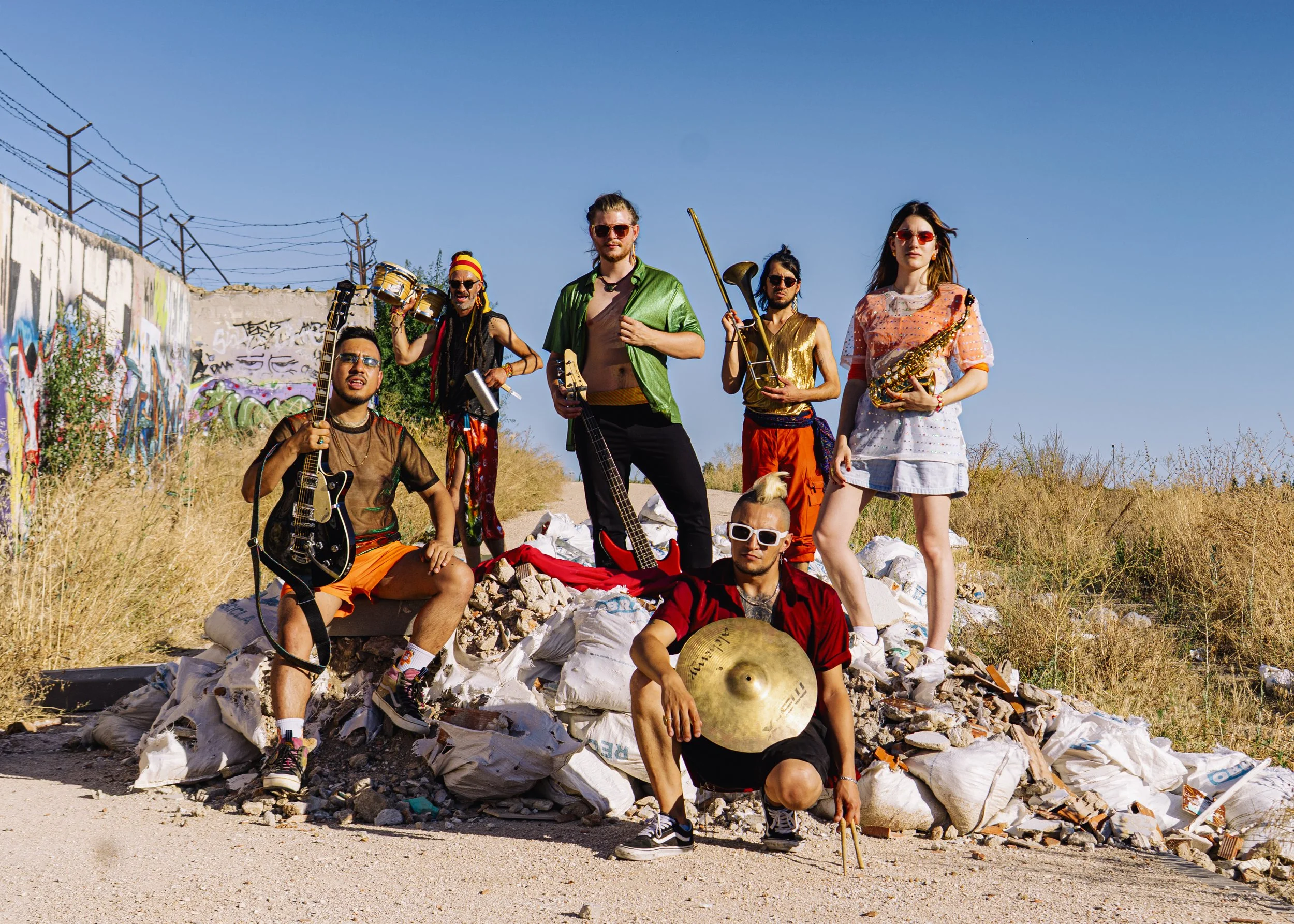 Un grupo de personas con instrumentos musicales en un entorno al aire libre, rodeados de basura y graffitis.