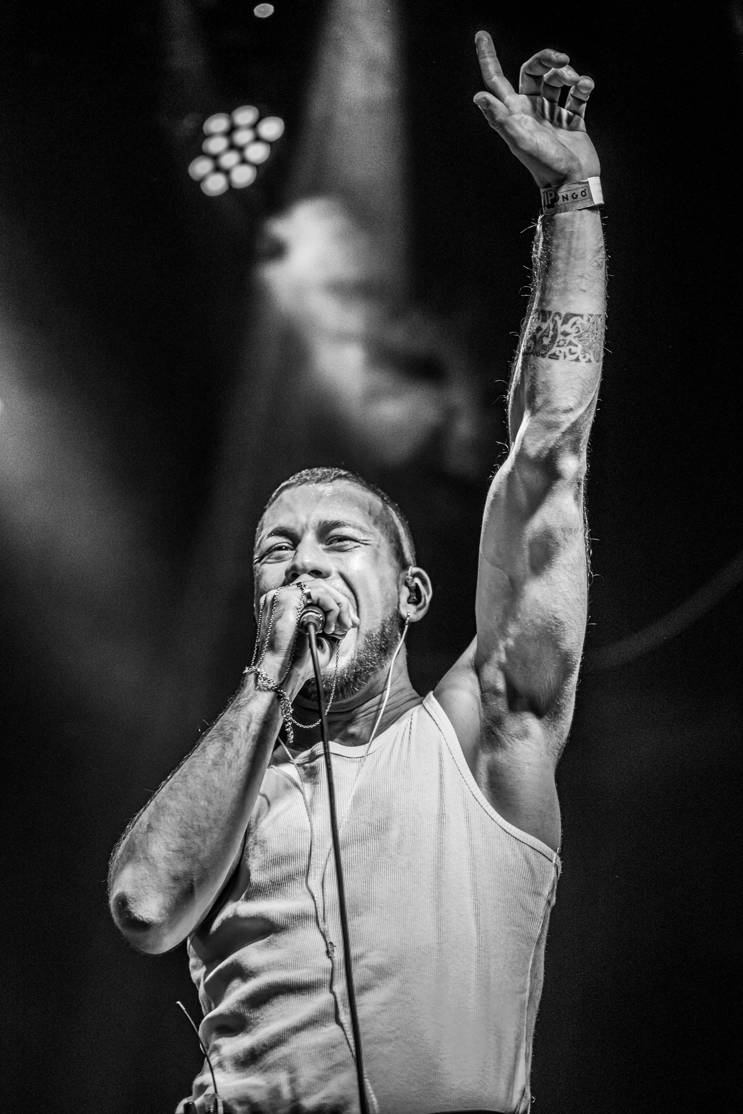 Joven cantante en concierto, sosteniendo un micrófono y levantando una mano, en un escenario con iluminación ajustada.