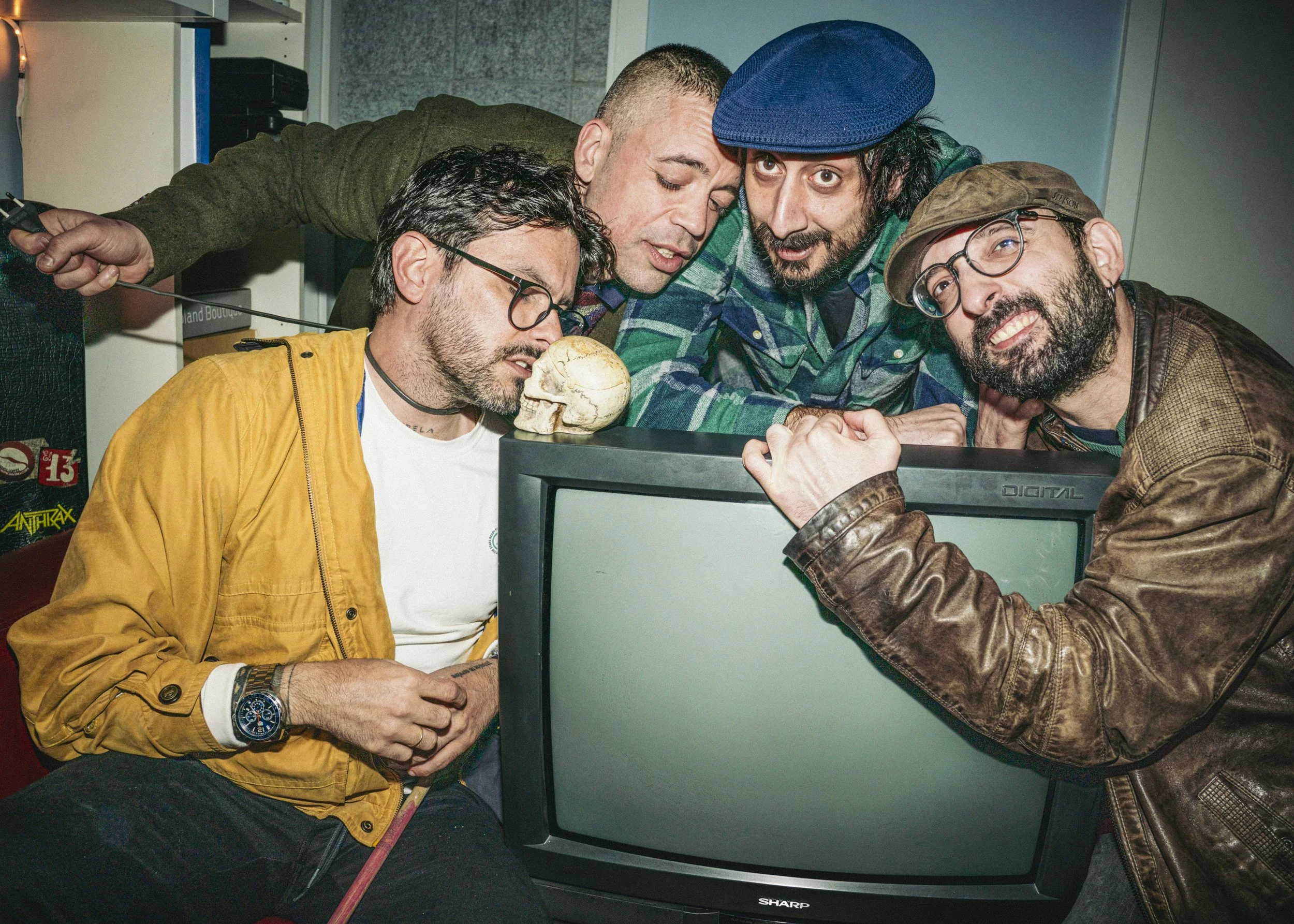 Cinco hombres con ropa casual observando y discutiendo sobre una televisión apagada en un entorno interior.