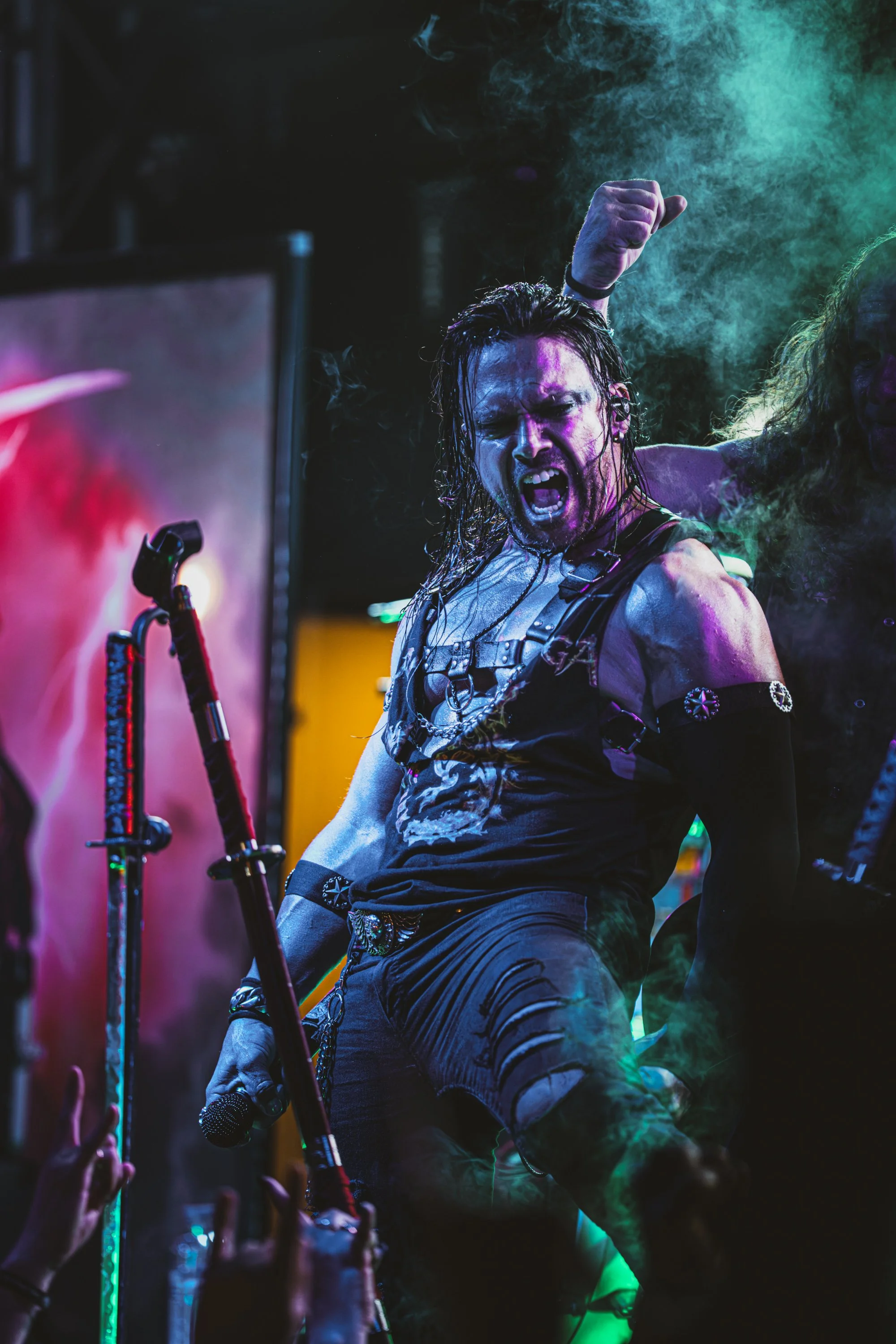 Persona con cabello mojado y expresión enérgica en concierto, rodeado de humo y luces de colores vibrantes.