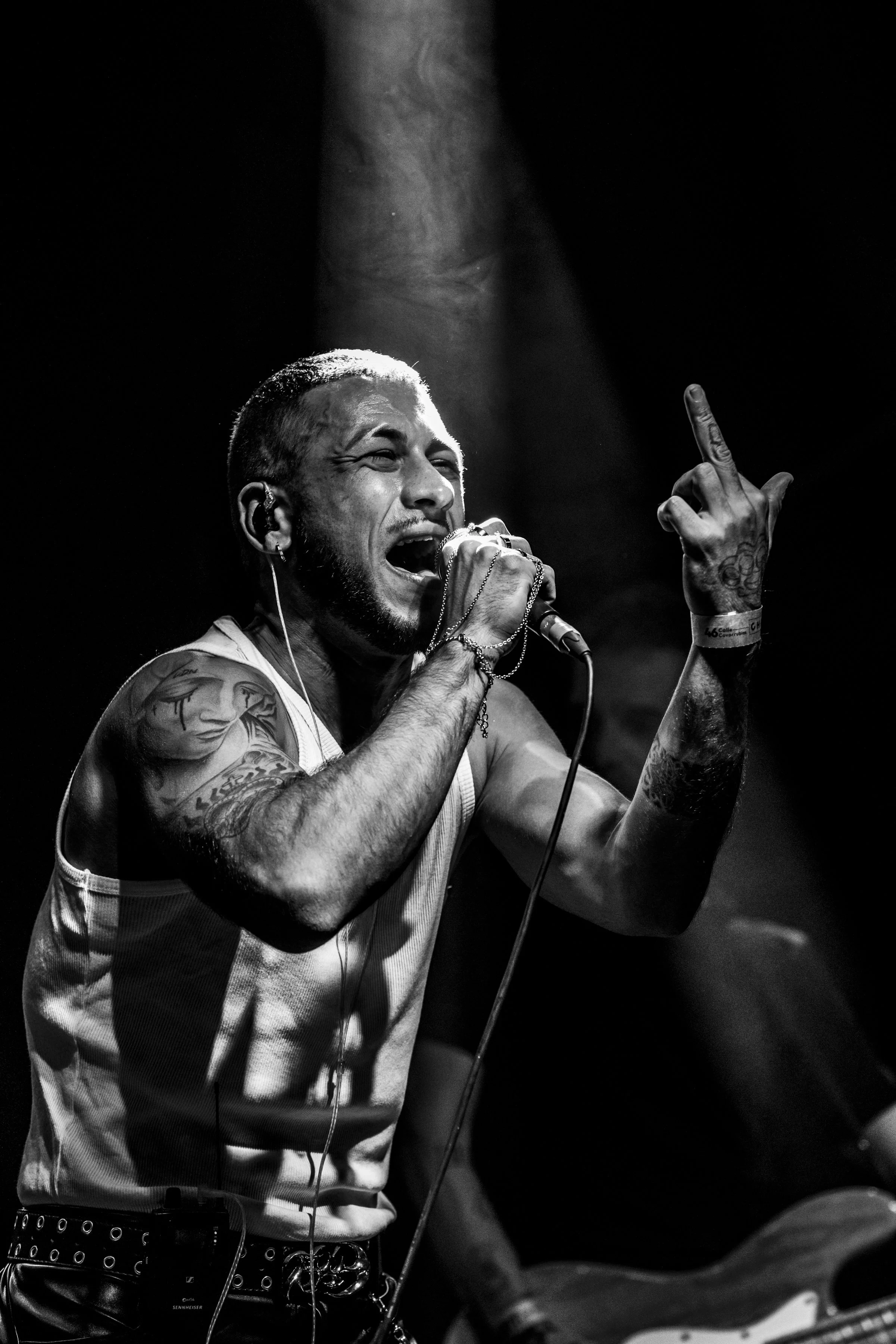 Hombre cantando en un concierto con tatuajes, sosteniendo un micrófono y haciendo un gesto con la mano