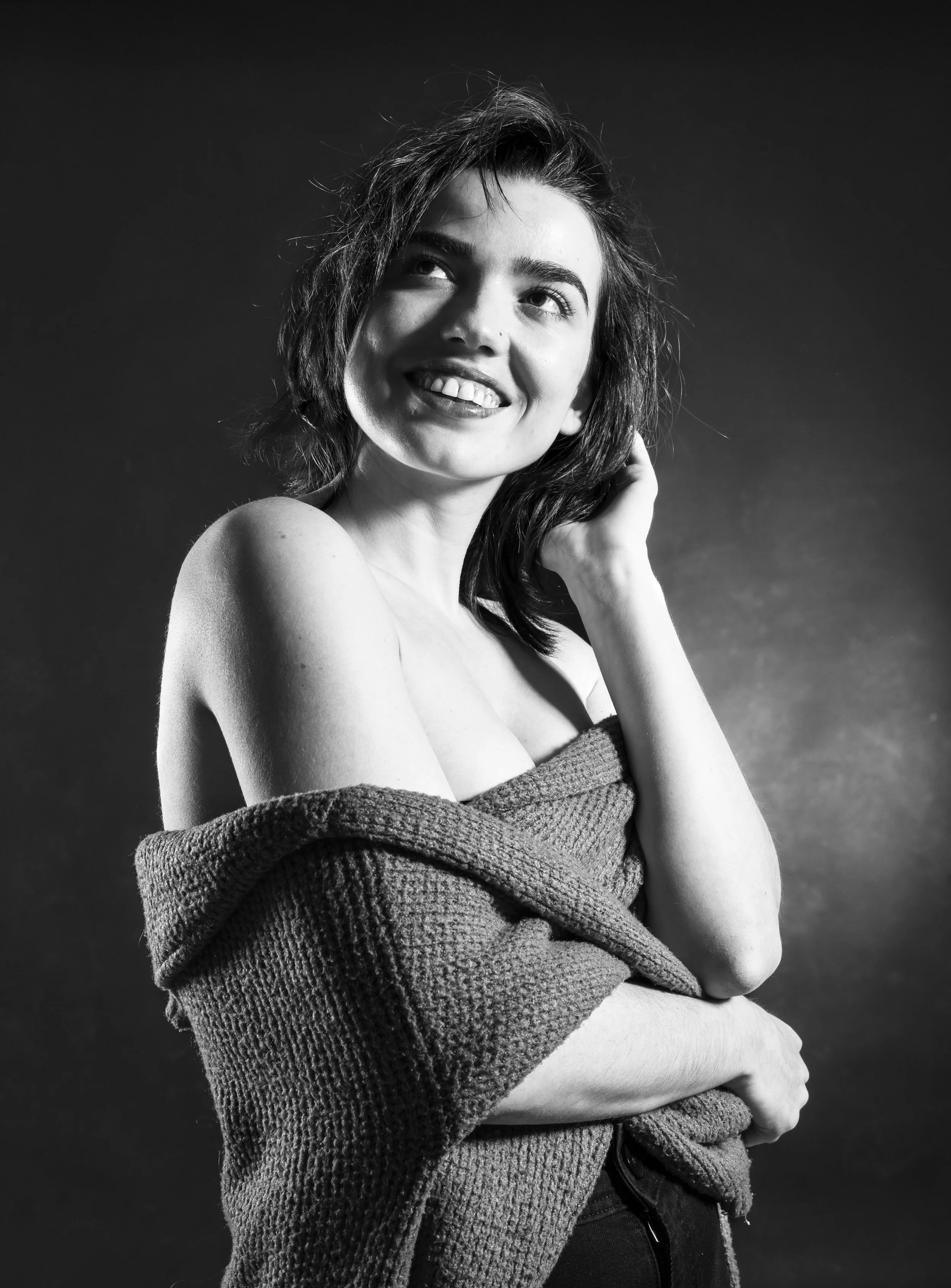 Retrato en blanco y negro de una mujer con cabello despeinado, sonriendo y tocándose el cabello, con una toalla enrollada alrededor de sus hombros.