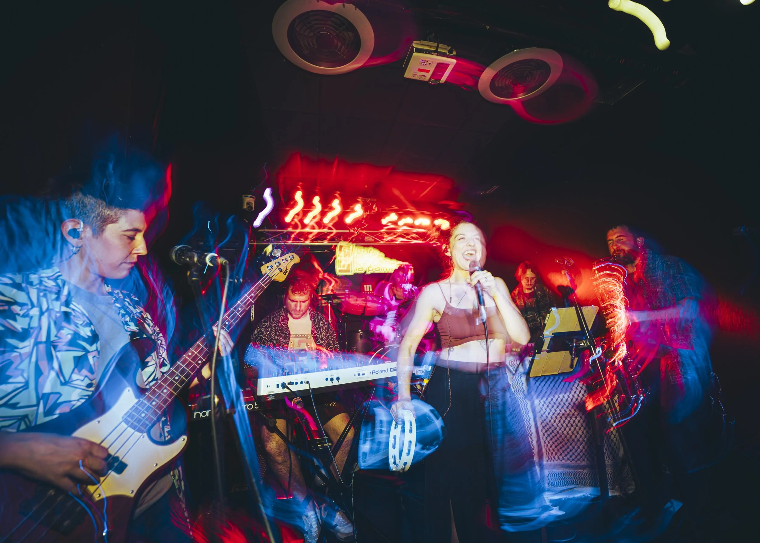 Un grupo de personas tocando instrumentos en un concierto en un escenario con luces de colores y ambiente vibrante.