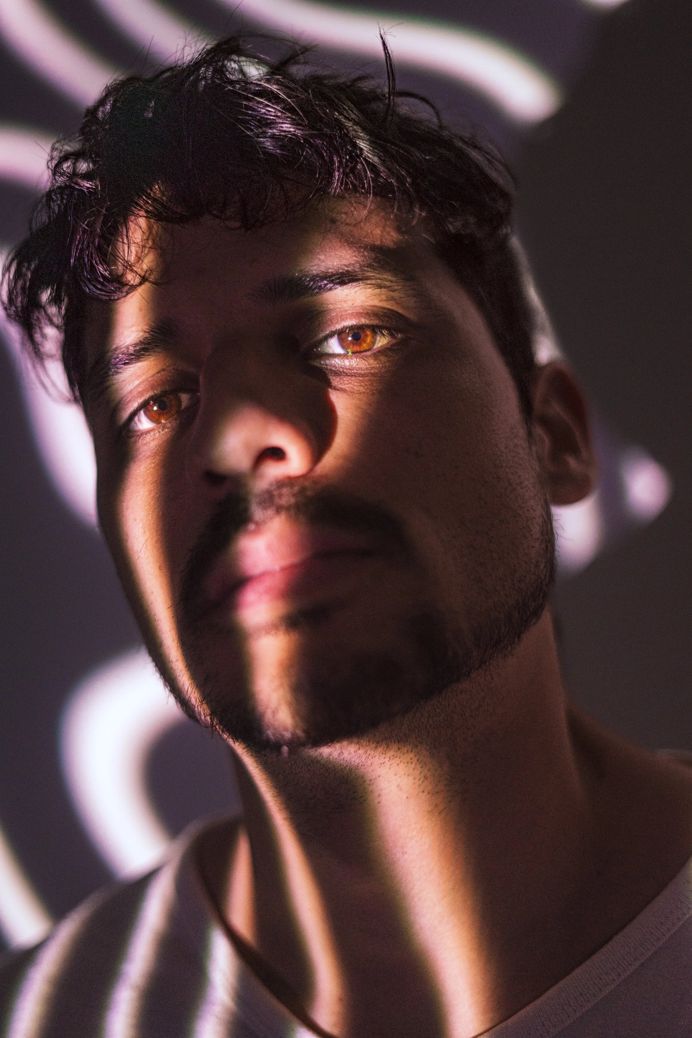 Retrato de un hombre con cabello oscuro y barba, con luz y sombras proyectadas en su rostro, en un fondo oscuro.