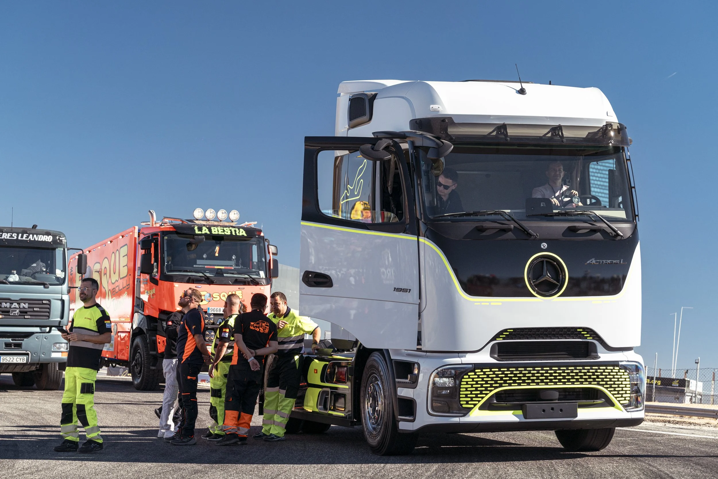 Grupo de personas con uniforme de emergencia junto a camiones, uno de ellos es un camión de rescate y otro un camión de transporte grande, en un área abierta bajo un cielo despejado.