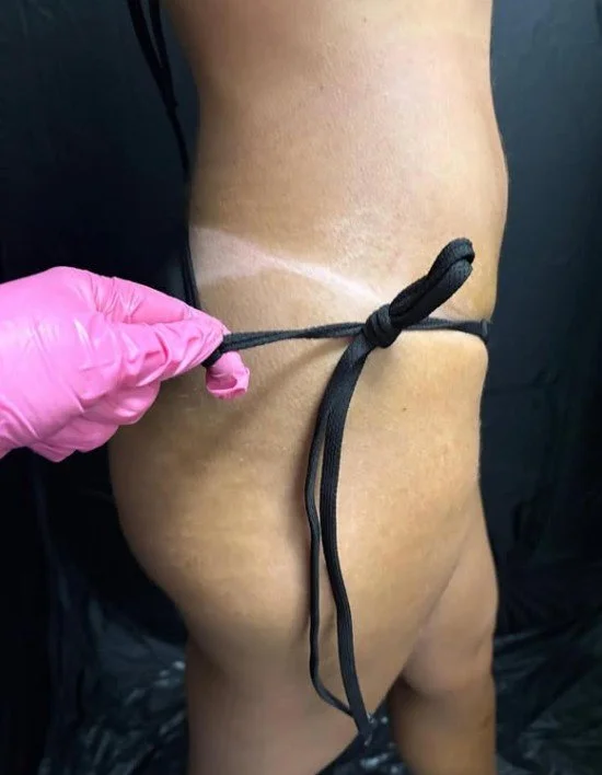 Person with a tan line around their waist, being tied with a black shoelace by a person wearing a pink glove.