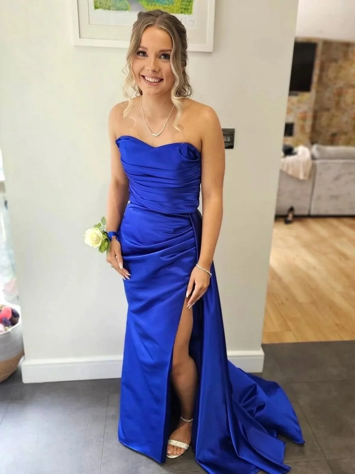 A young woman in a strapless royal blue gown with a high slit, standing indoors and smiling at the camera.