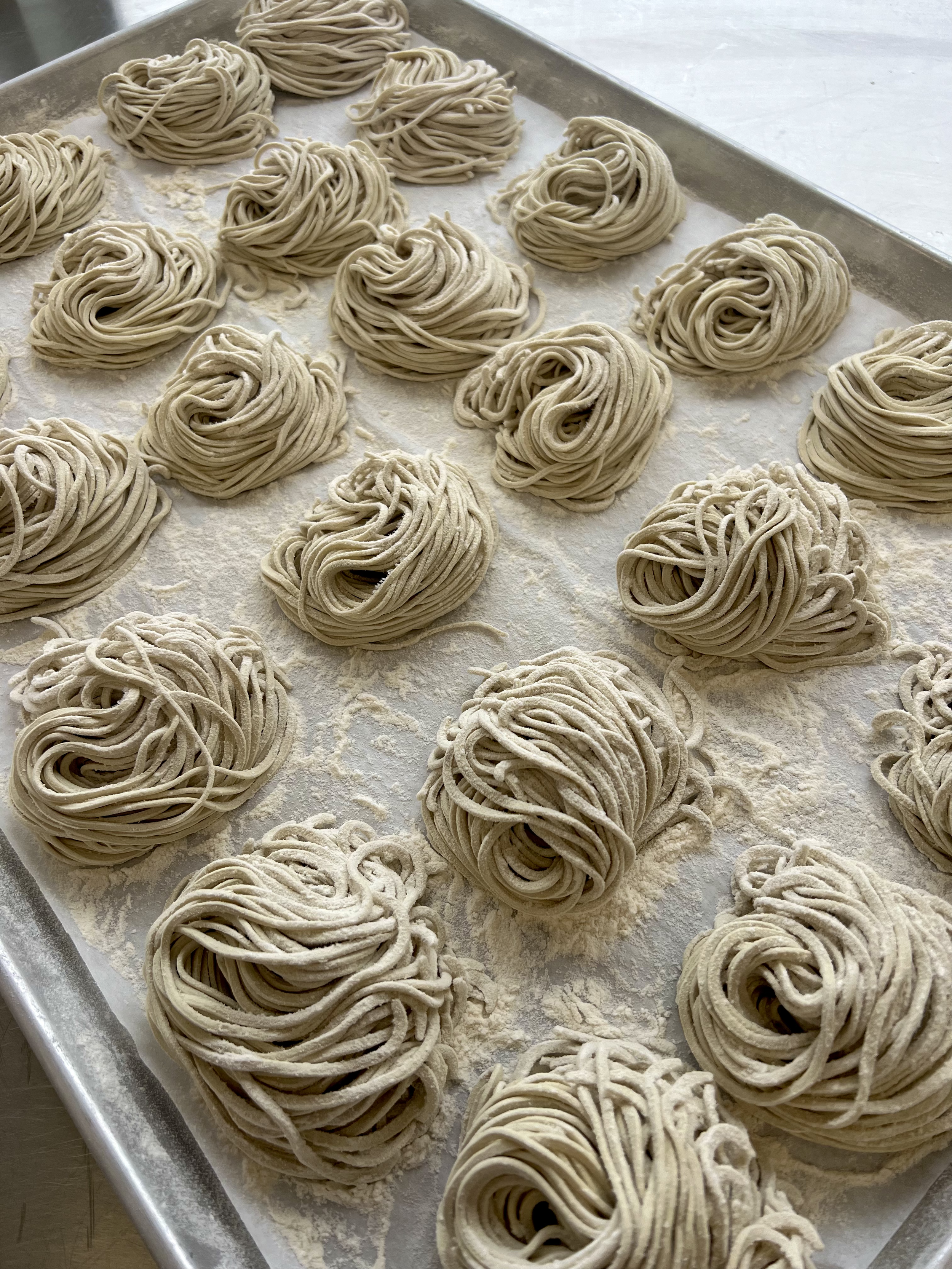 Multiple nests of uncooked pasta, likely spaghetti or similar, on a floured baking sheet.