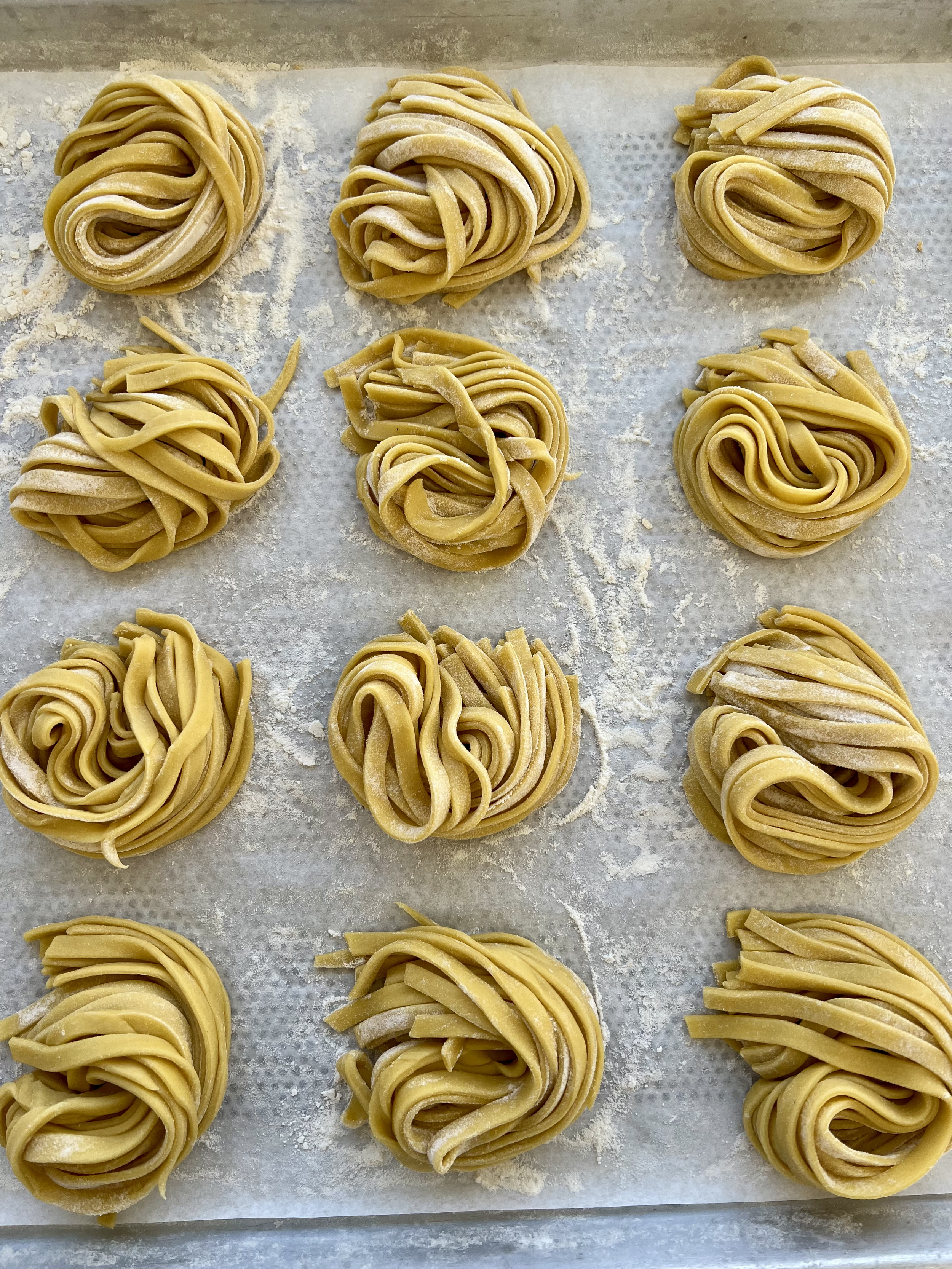 Arranged raw pasta nests on a floured baking sheet.