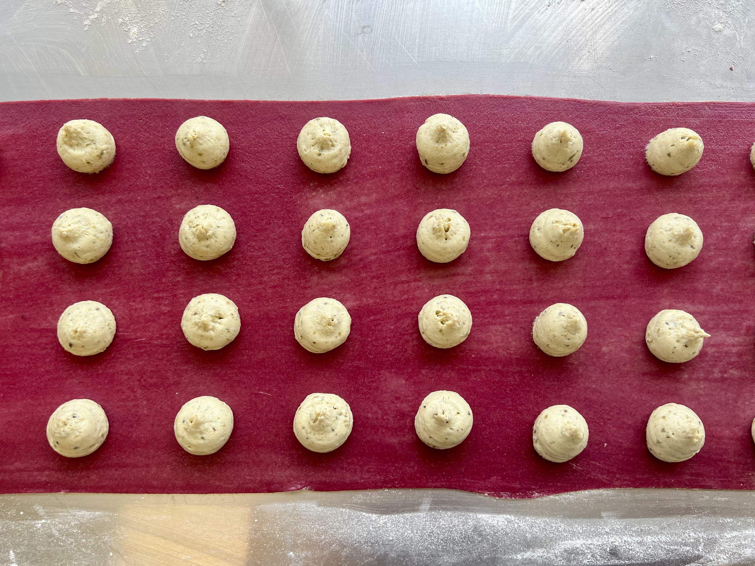 Rows of small round cookie dough balls on a red silicone baking mat.