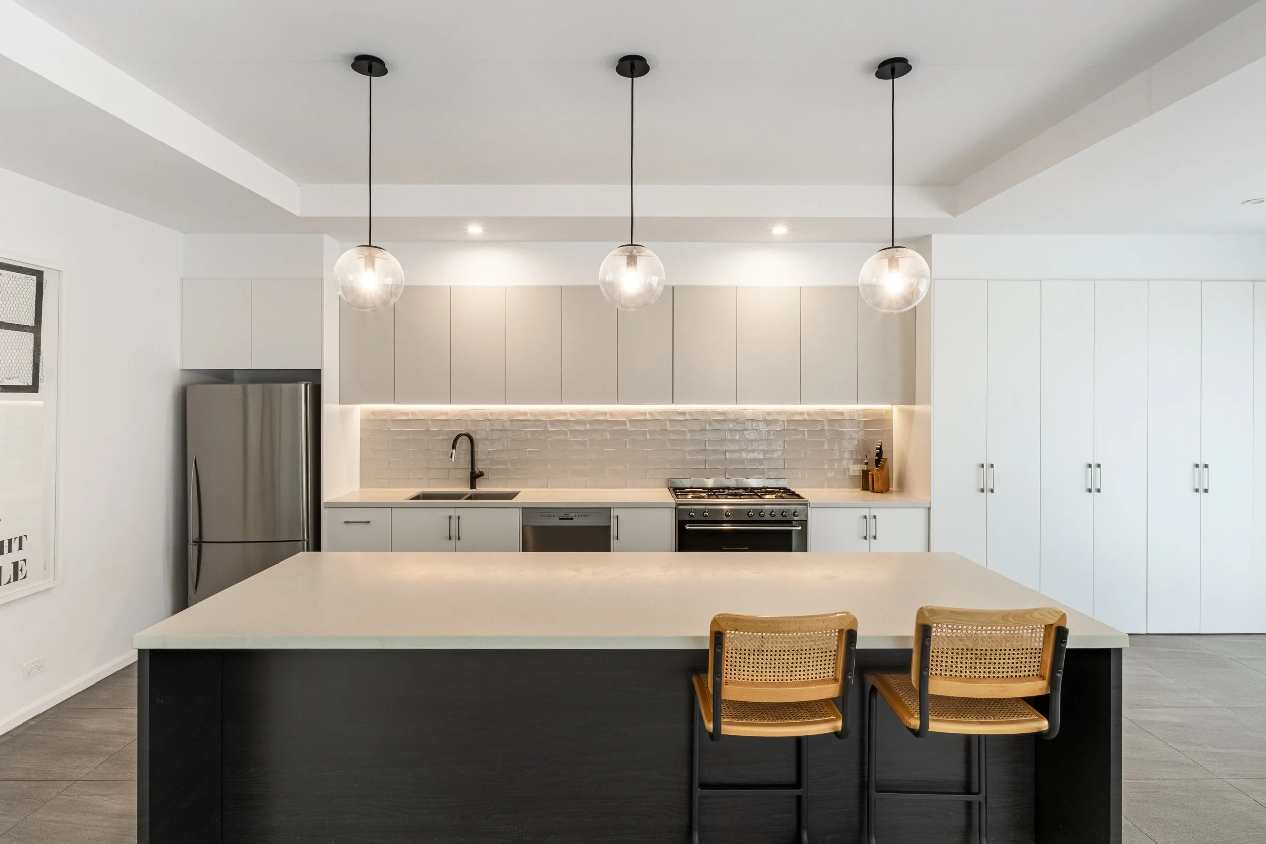 Modern kitchen with white cabinets, a black countertop island, a stainless steel refrigerator, and three hanging globe pendant lights.