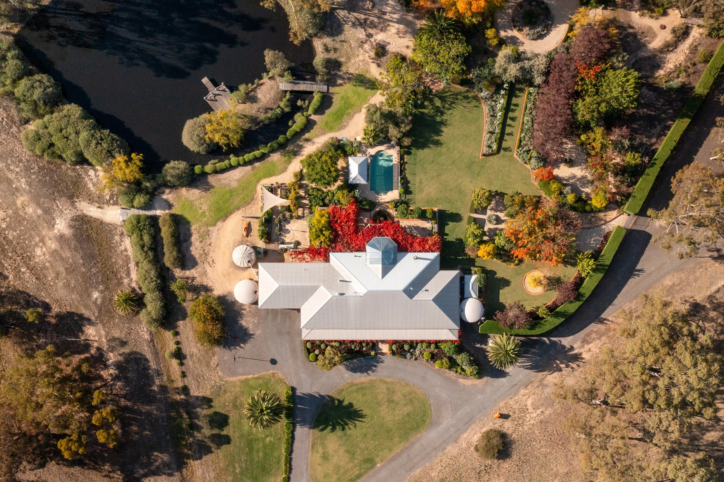 An aerial view of a residential property with a large house, swimming pool, and lush landscaped yard, surrounded by trees and a winding driveway.