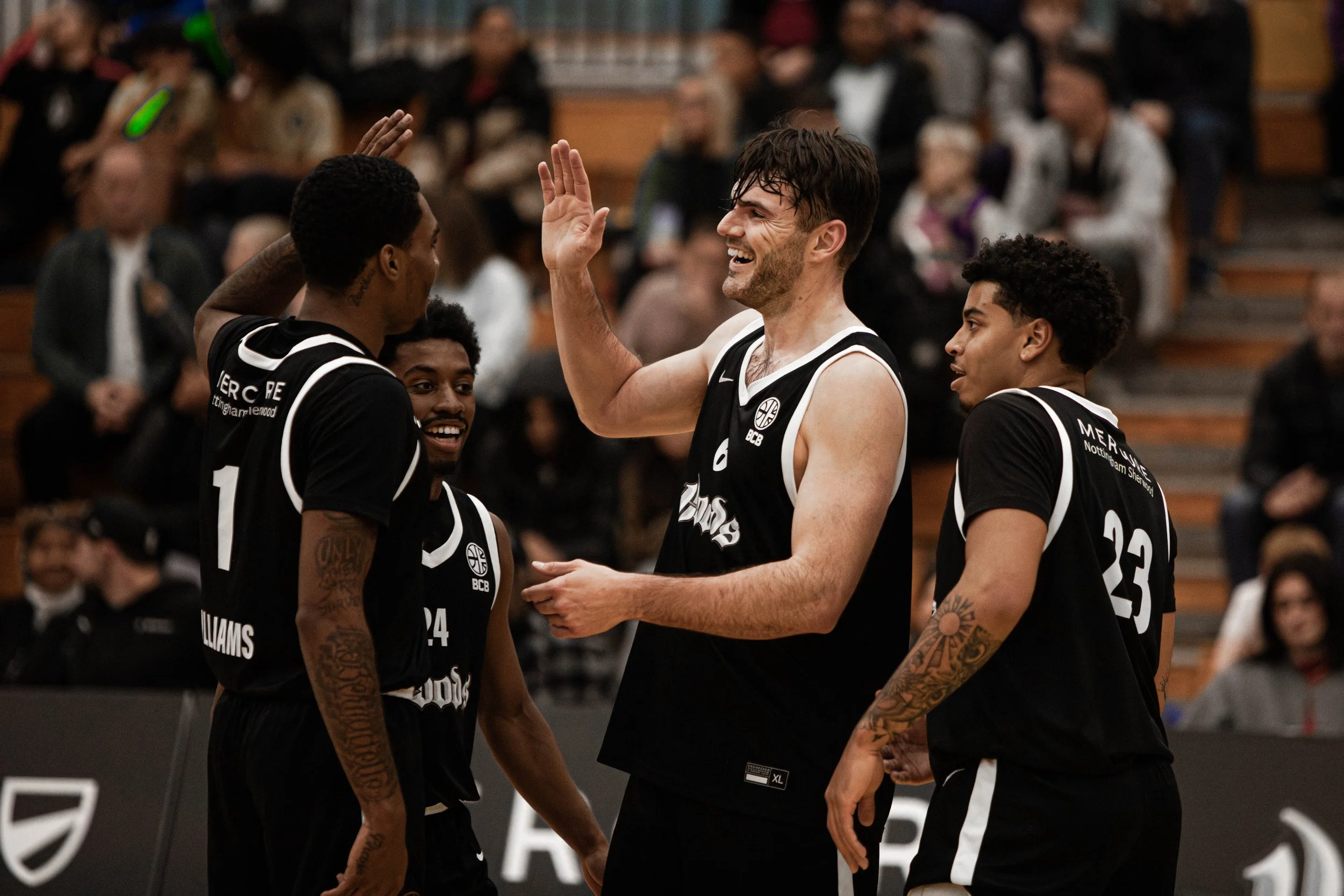 Group of basketball players in black jerseys celebrating during a game, with one player smiling and giving a high five.