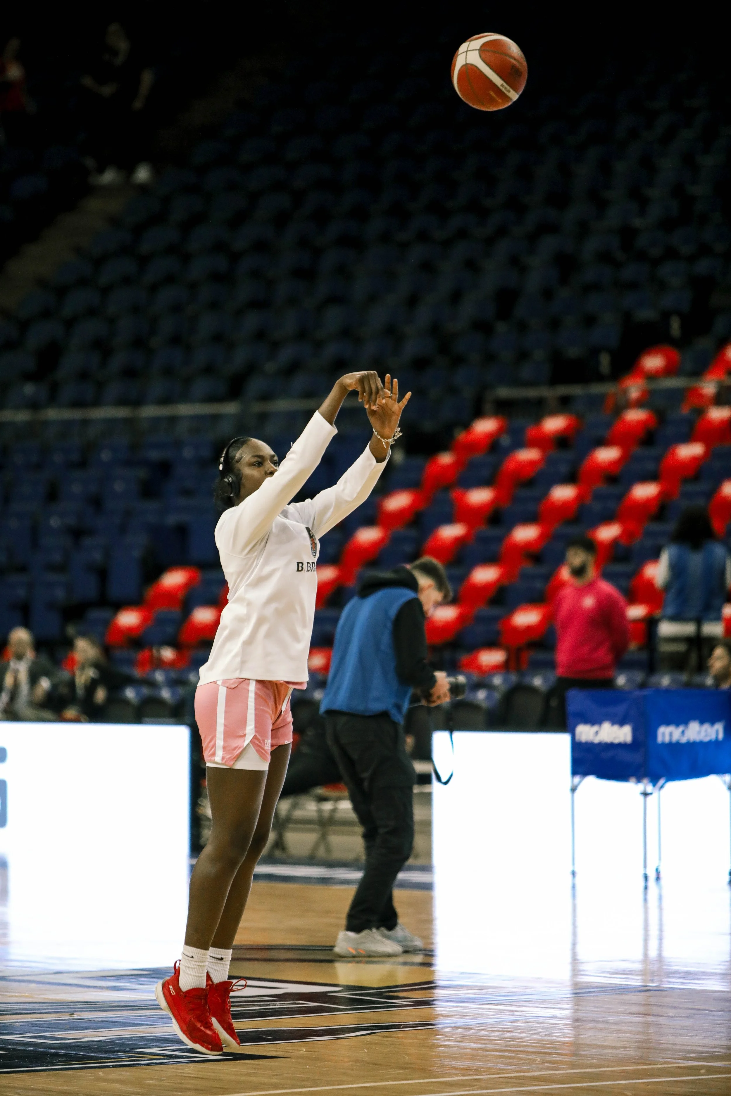 A female basketball player is shooting a basketball during a practice or warm-up in an indoor arena.