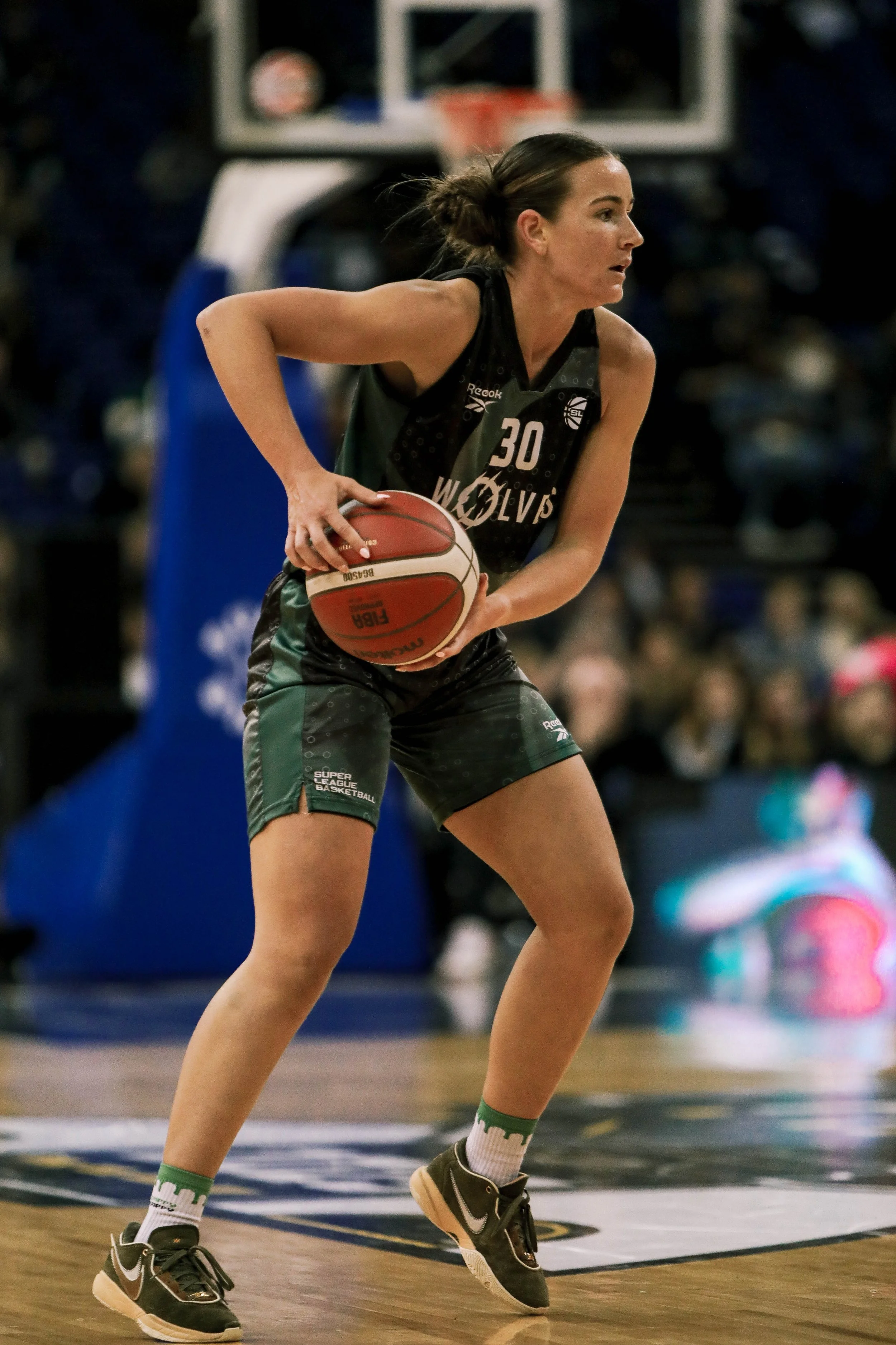 Female basketball player in black team uniform holding a basketball on a game court.