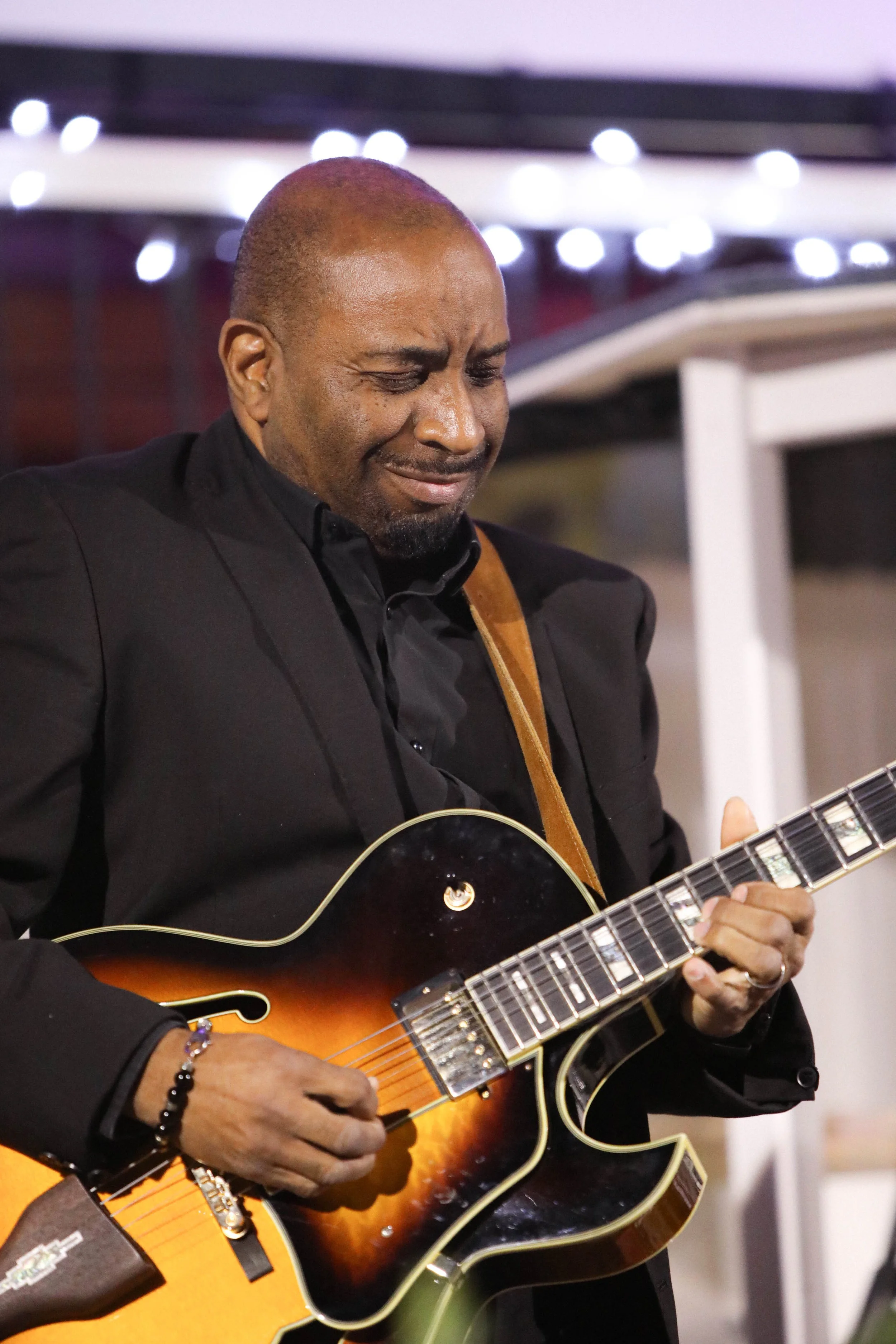 Man in black suit playing an acoustic guitar while performing.