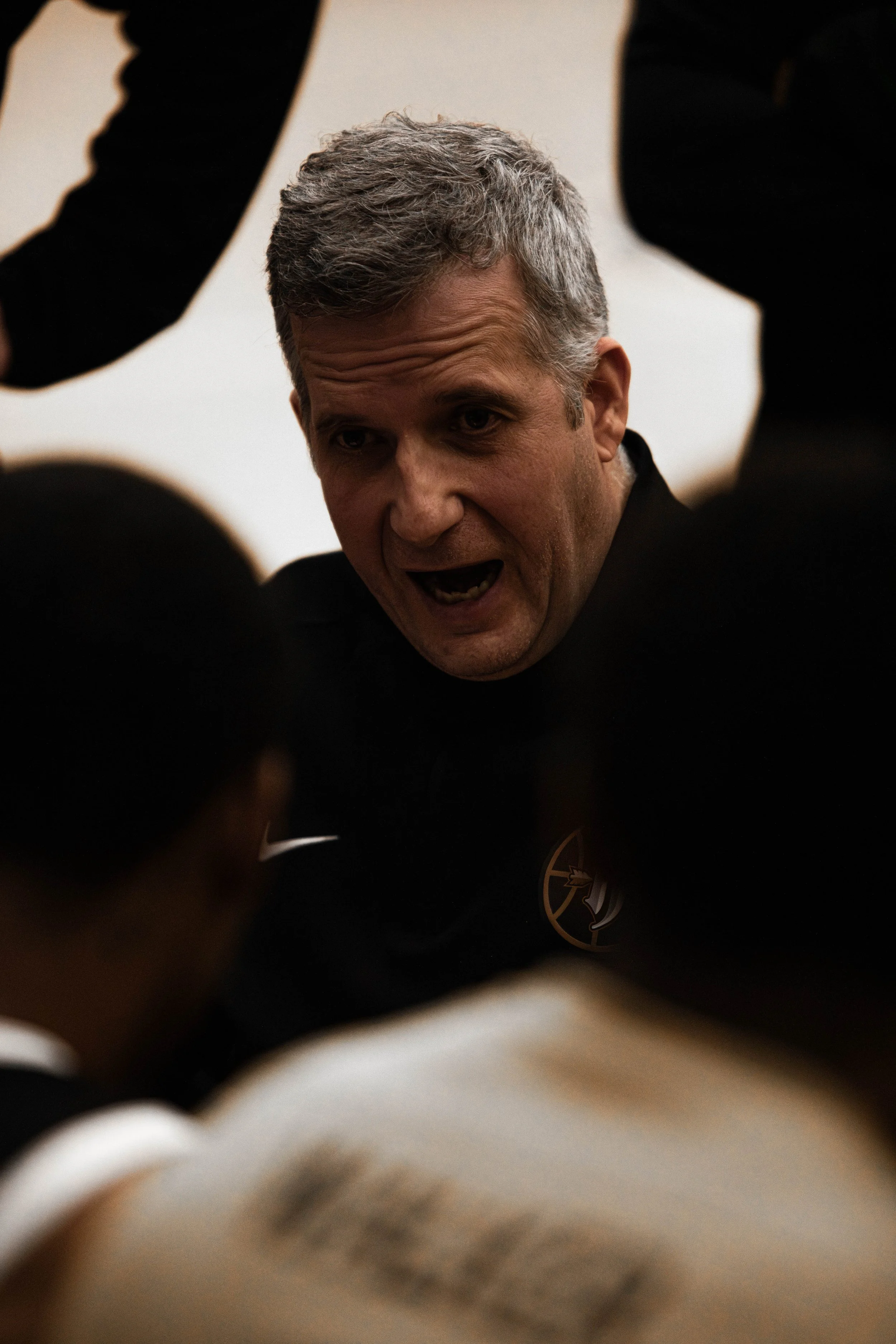 A man speaking passionately, surrounded by others in a group, in an indoor setting.