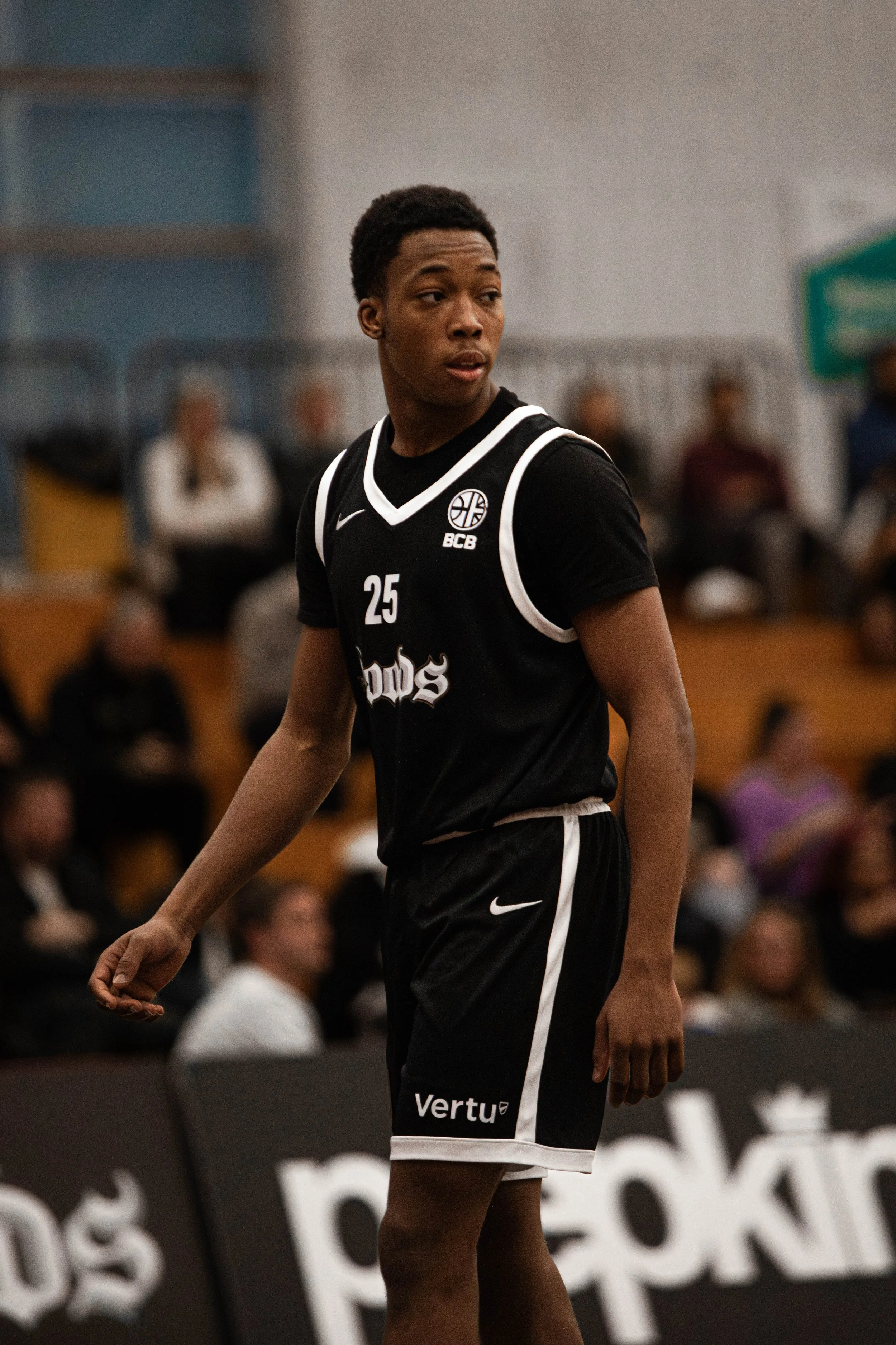 A young male basketball player wearing a black jersey with number 25 and seated on a basketball court.