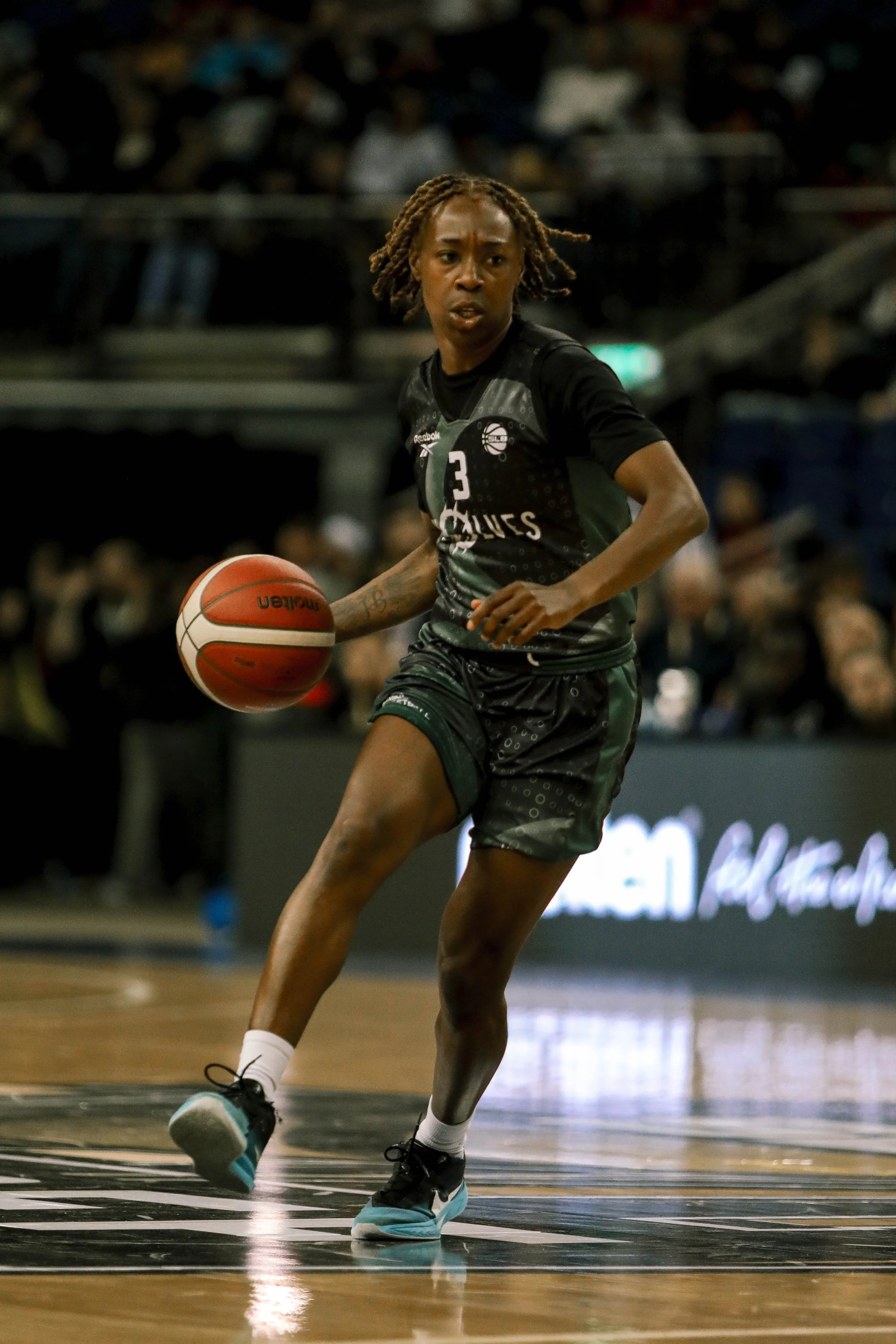 A female basketball player in black uniform dribbling a basketball on the court during a game.