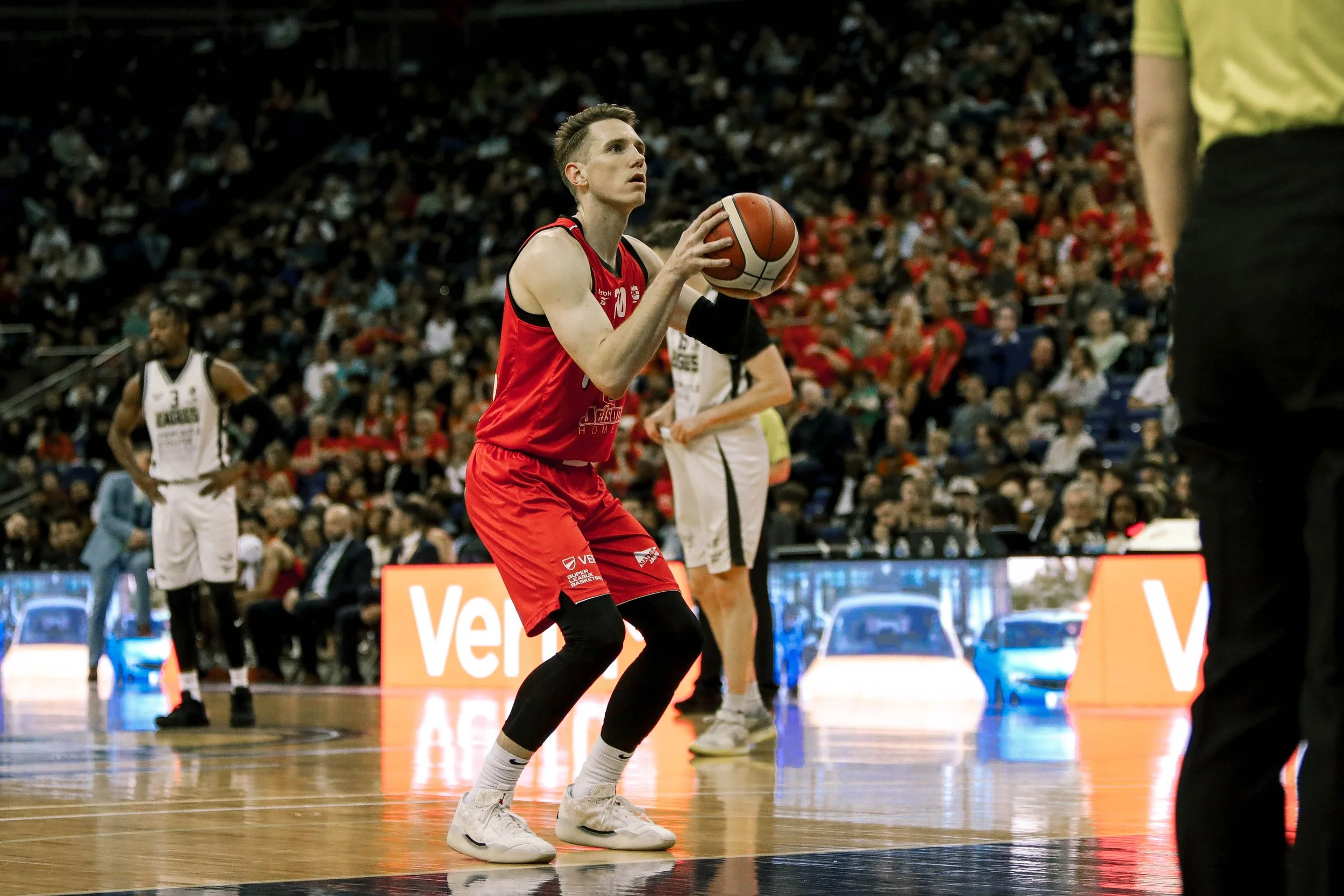 A basketball player in a red jersey prepares to shoot during a game with a crowd in the background.