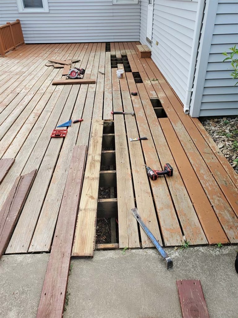 Construction of a new wooden deck with tools and partially assembled wooden planks. Hole cutouts for future supports or fixtures.