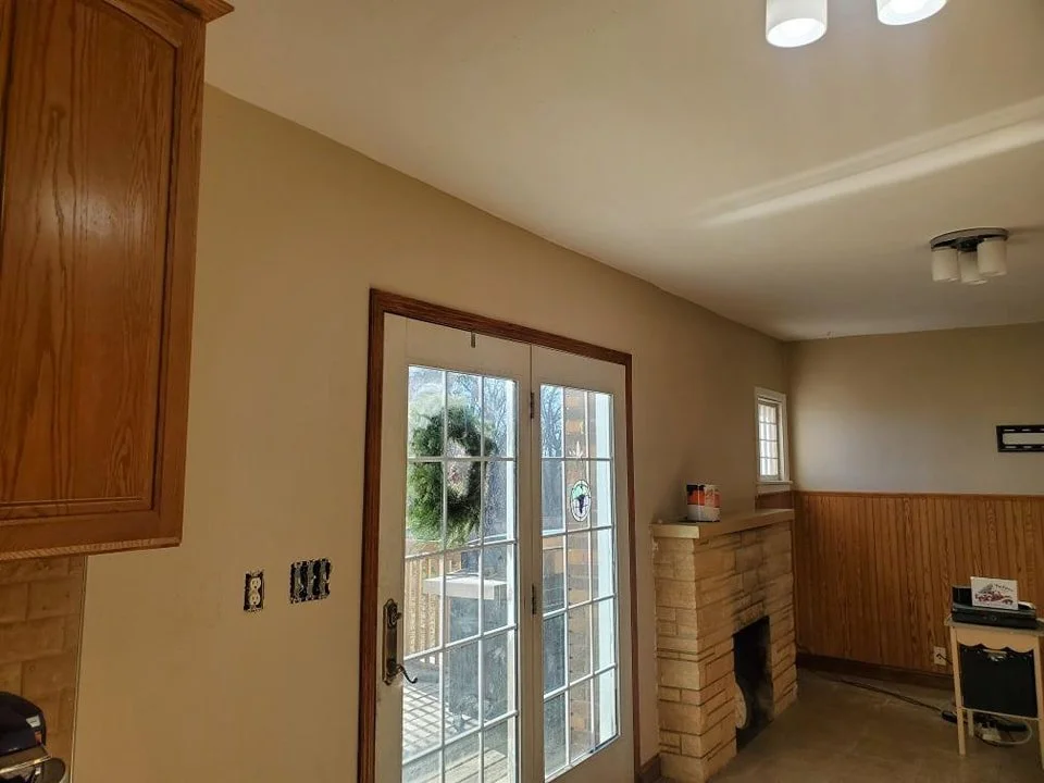 Interior of a room with a sliding glass door leading outside, a brick fireplace, wooden paneling on one wall, and a partial view of a small window.