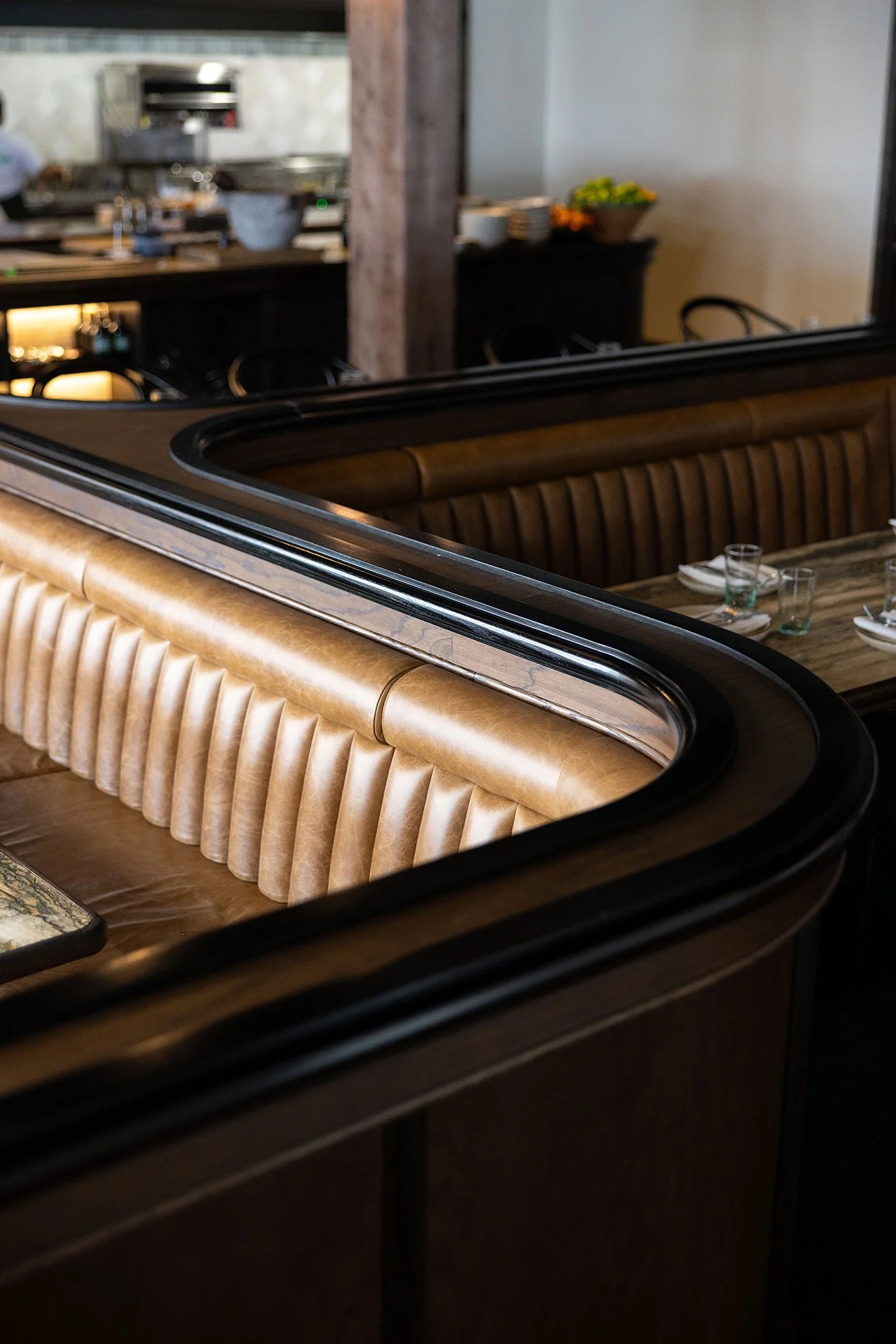 Close-up of a restaurant booth seating area with brown leather upholstery and a wooden table, in a dining area with place settings and glassware.