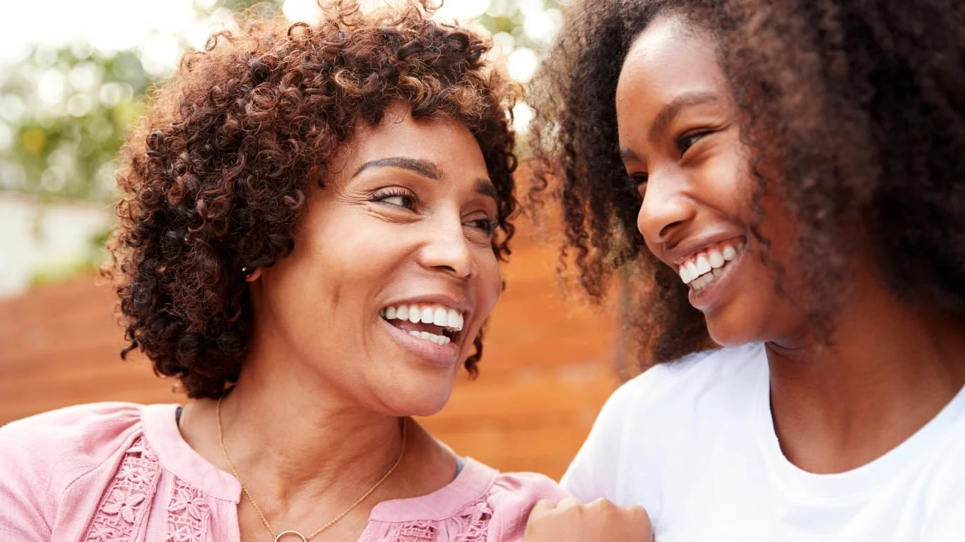 wo women laughing closely together outdoors, representing identity and family boundaries therapy in Connecticut